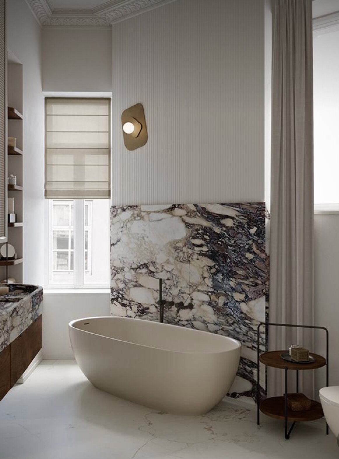 freestanding bathtub with marble wainscoting and modern wall sconce