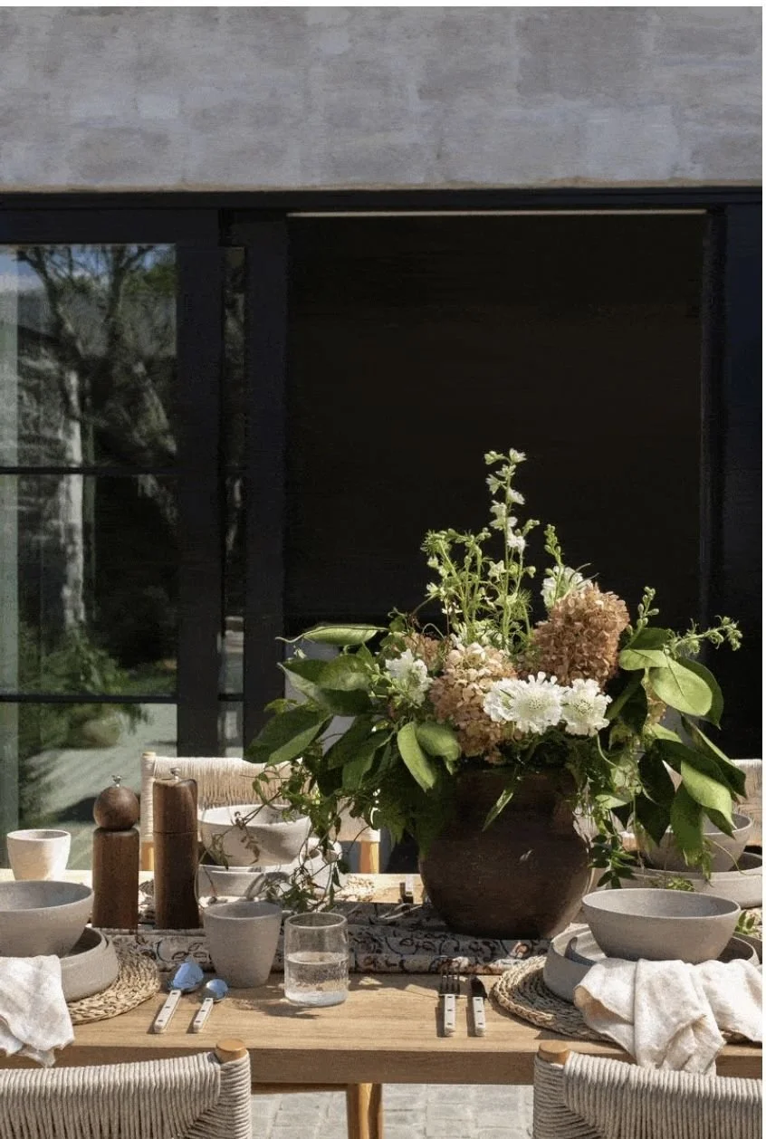 outdoor dining table styled with hand crafted ceramics, woven placemats, linen napkins and large eartheware