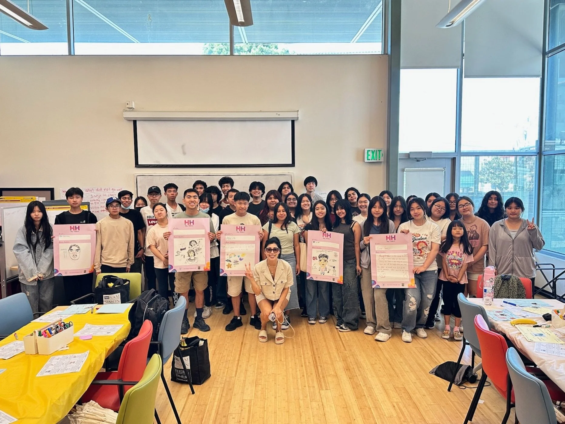 Group of students and a teacher in a classroom, holding posters for a Hey Haters Youth Program