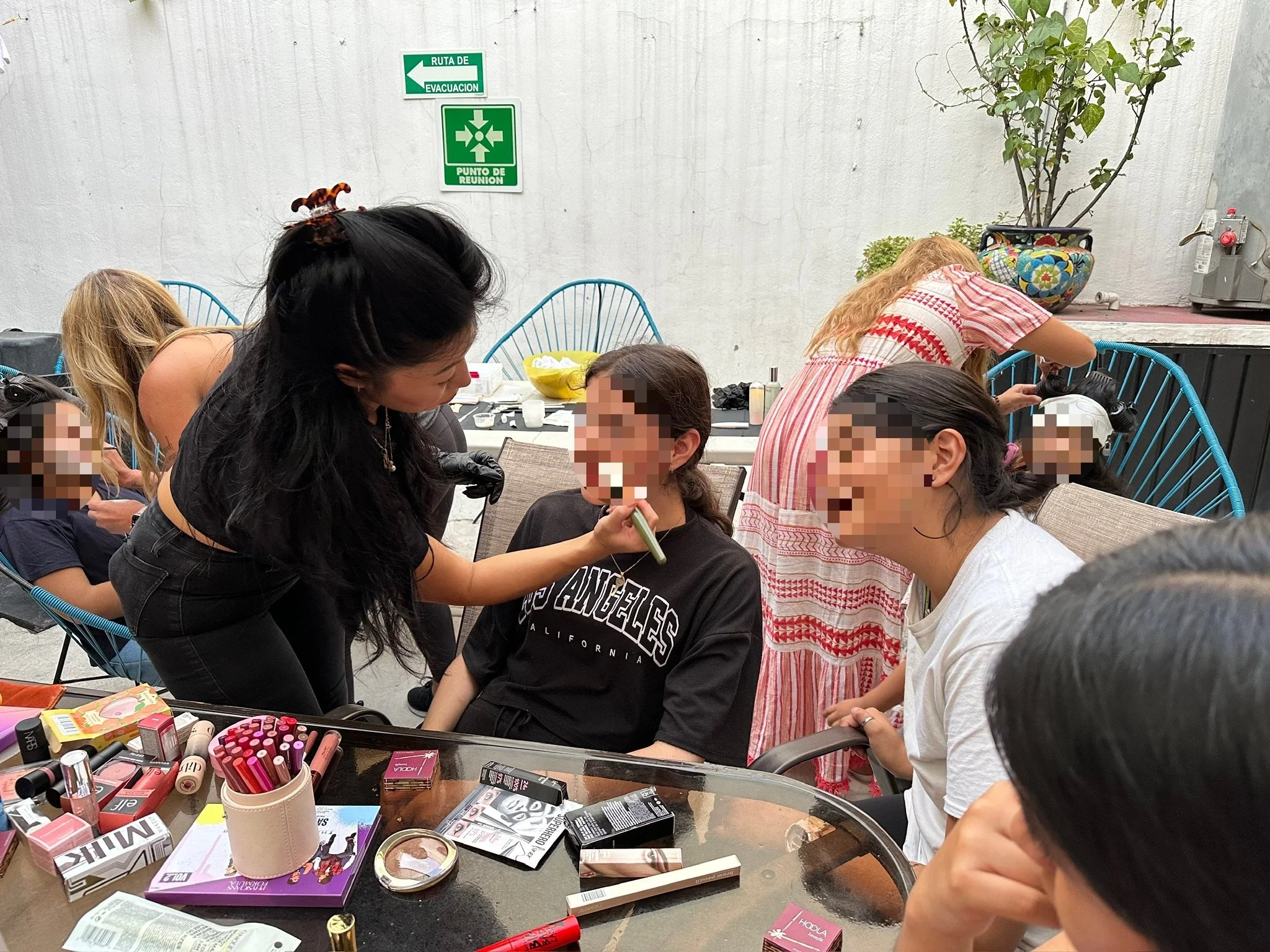 Group of women and children gathered around a table outdoors, participating in a beauty activity, with makeup supplies and beauty products on the table for survivors of Trafficking.