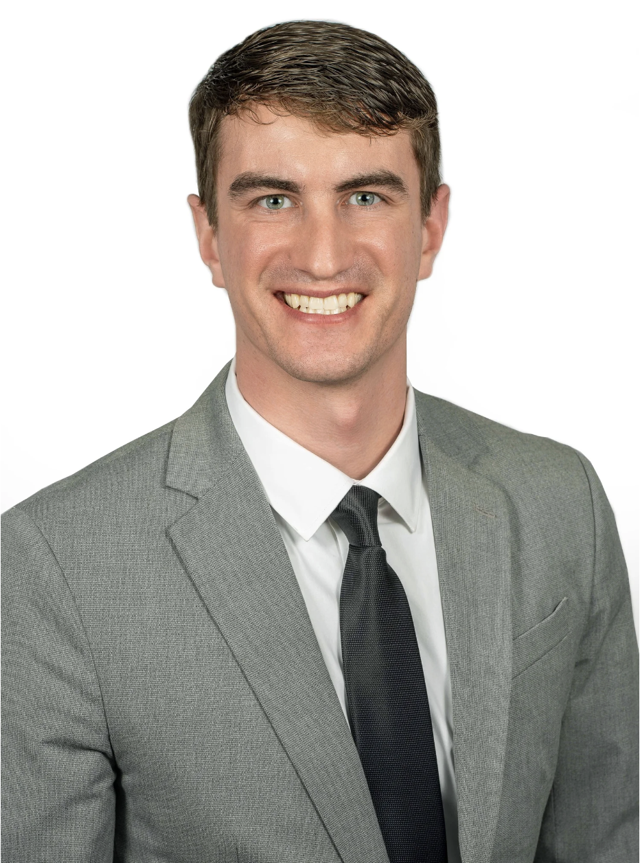 A young man with short brown hair, blue eyes, and a big smile, dressed in a gray suit, white shirt, and black tie, against a plain white background.