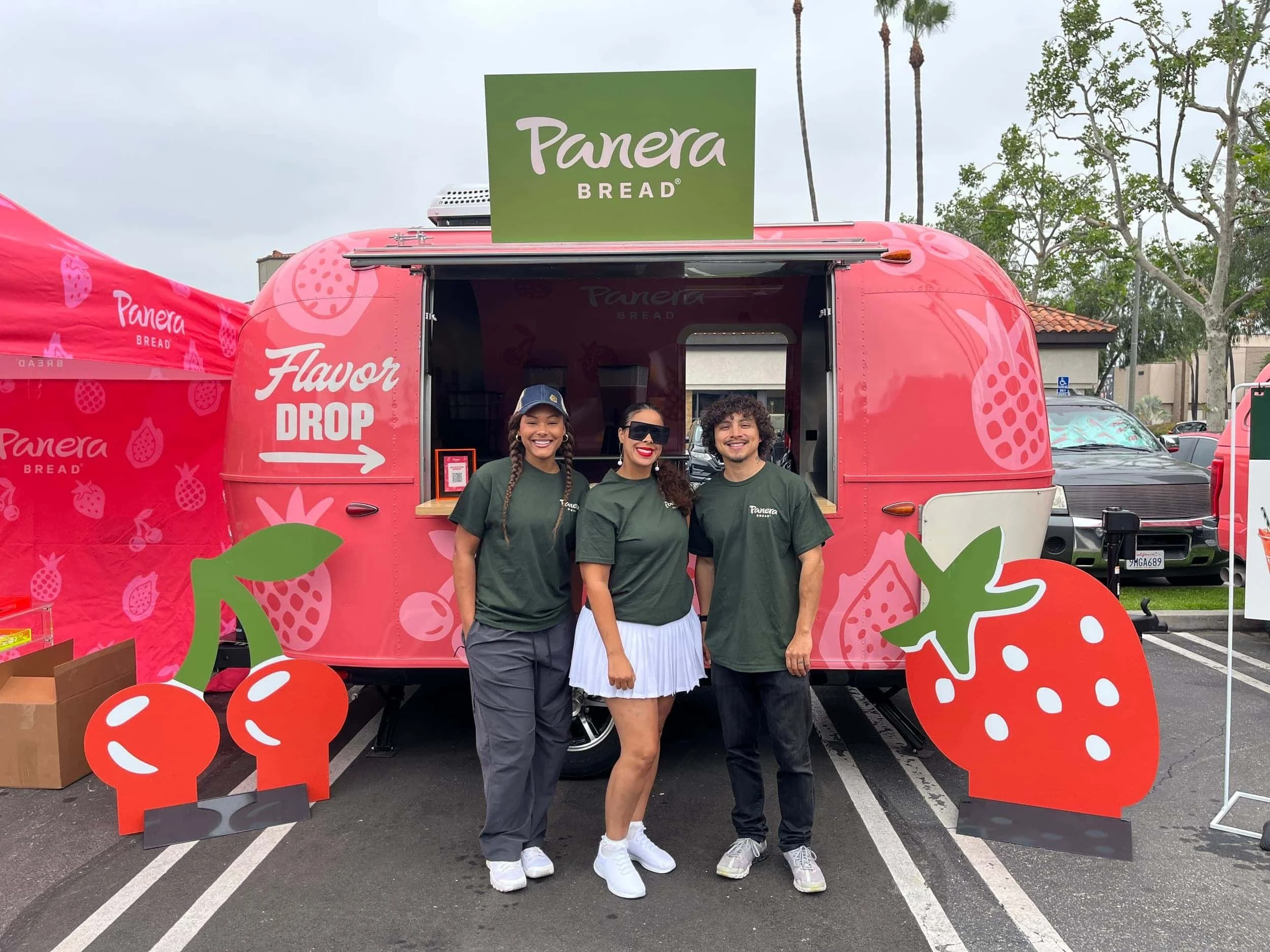 Three Panera Bread team members smiling in front of a pink Flavor Drop food truck decorated with fruit graphics at an outdoor event - Encore Nationwide