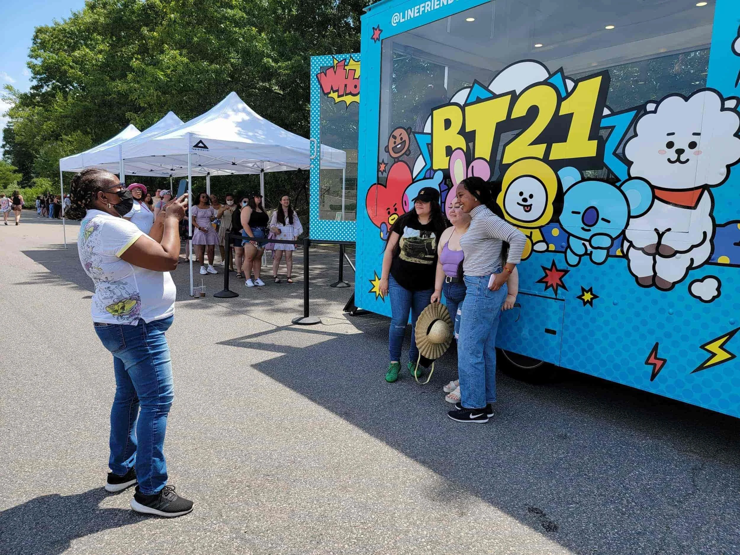 Fans posing for a photo in front of a colorful BT21 pop-up truck at an outdoor promotional event