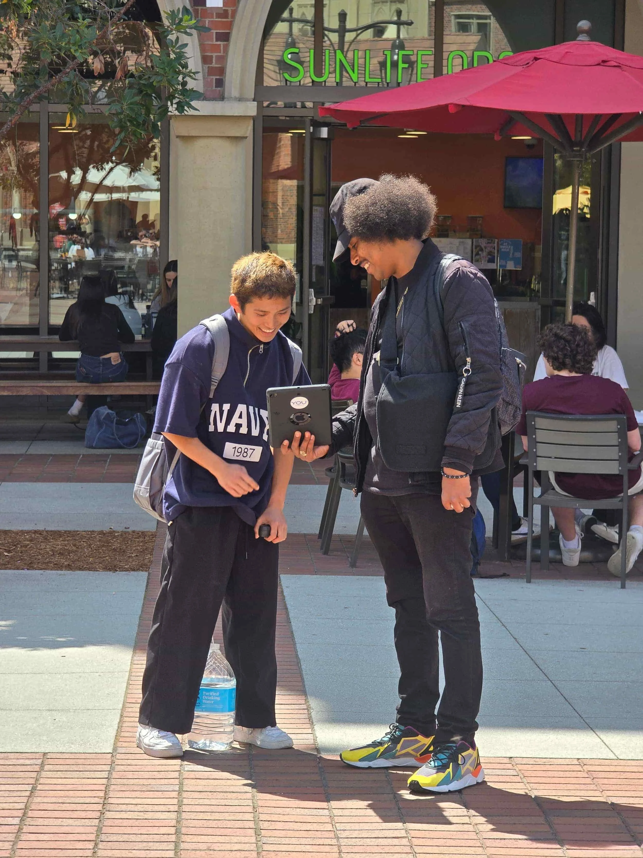Two young men standing outdoors on a patio looking together at a tablet screen outside SunLife Organics
