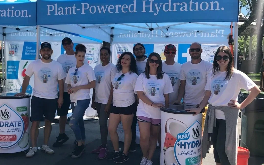 V8 +HYDRATE promotional event team posing under a Plant-Powered Hydration branded canopy tent