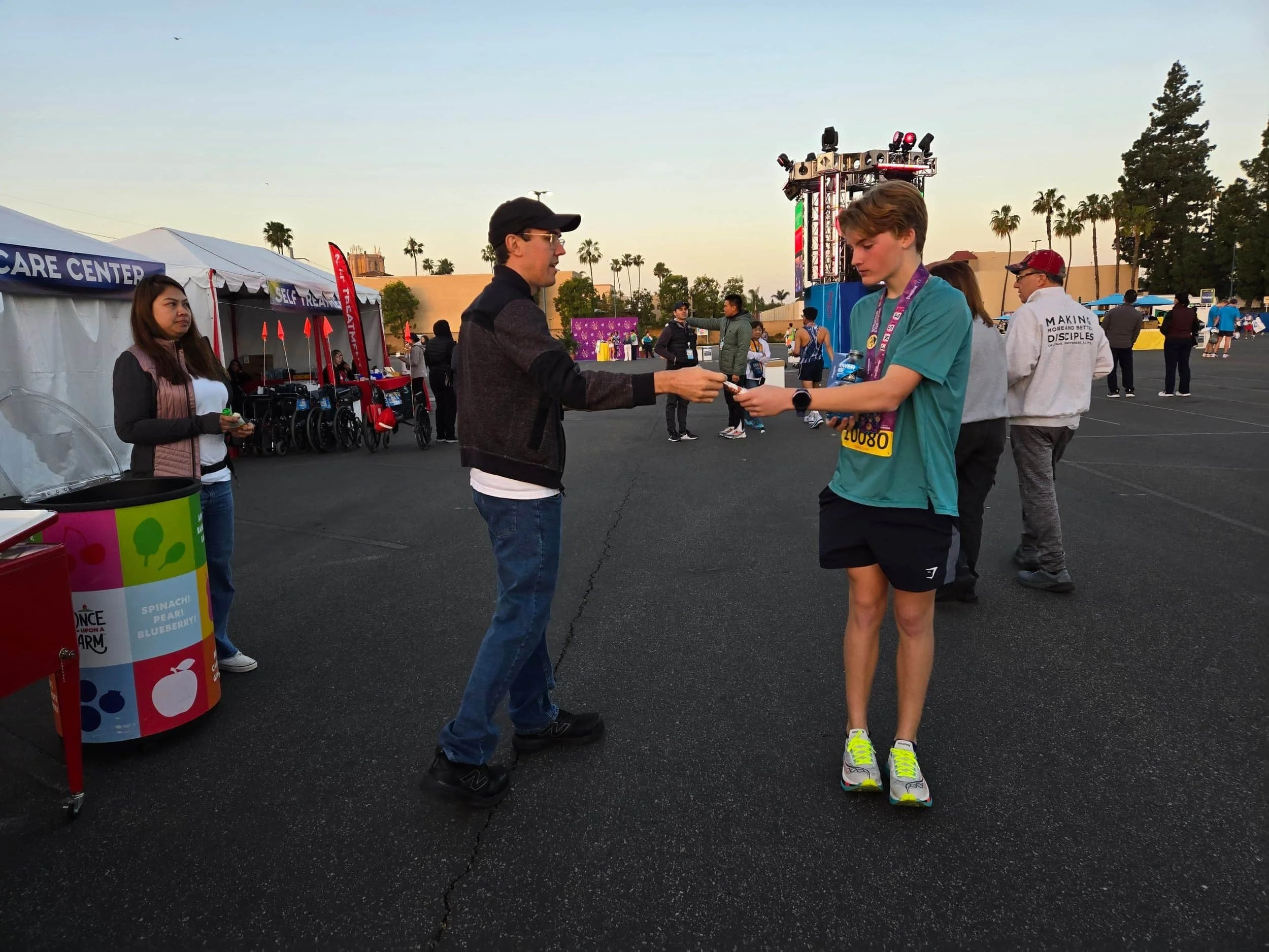 A young runner with a race medal receiving a sample outside a medical tent at an outdoor marathon finish line