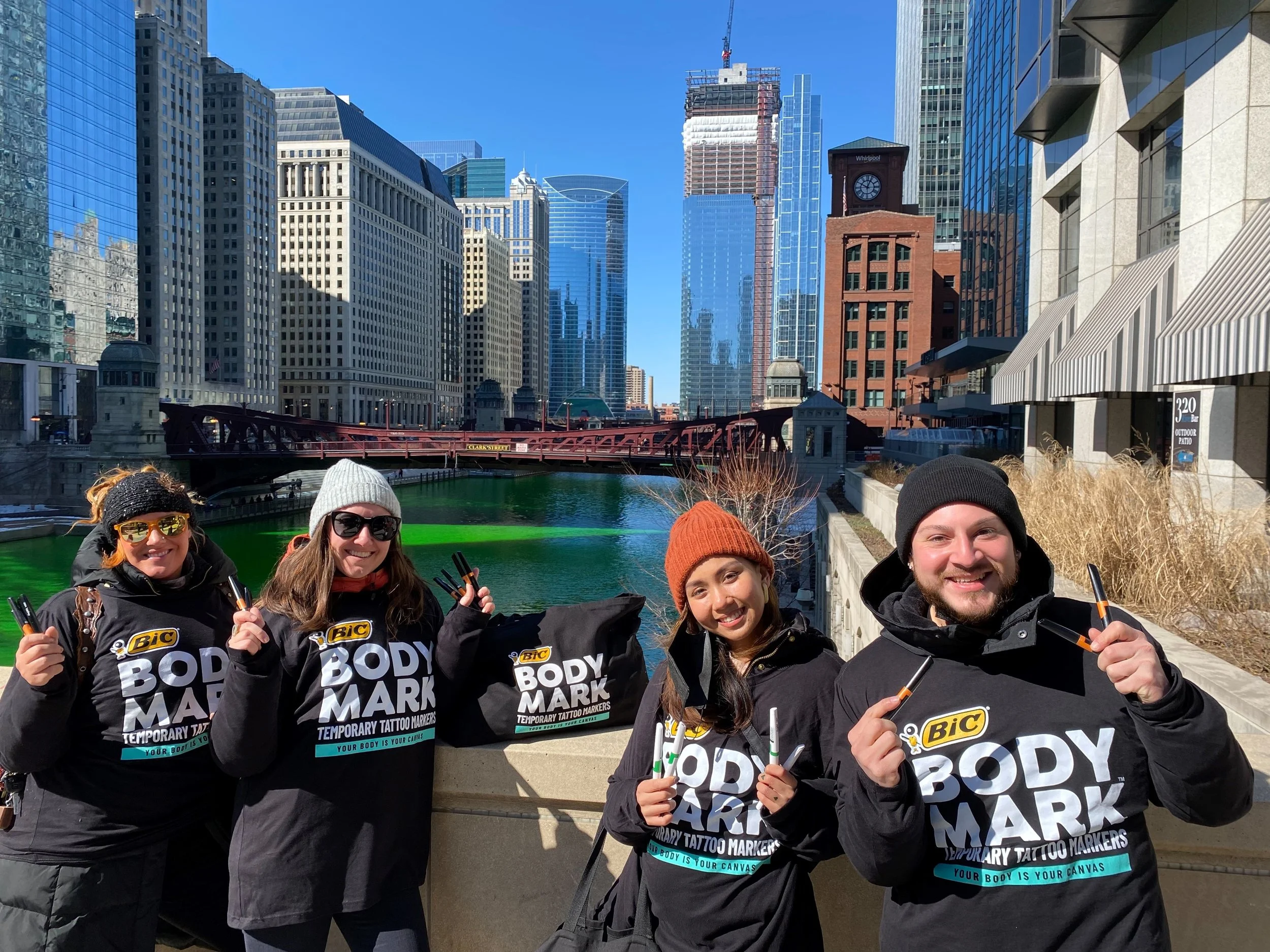 BIC BodyMark brand ambassadors and event staff holding temporary tattoo markers posing by a river in front of city skyscrapers - Encore Nationwide