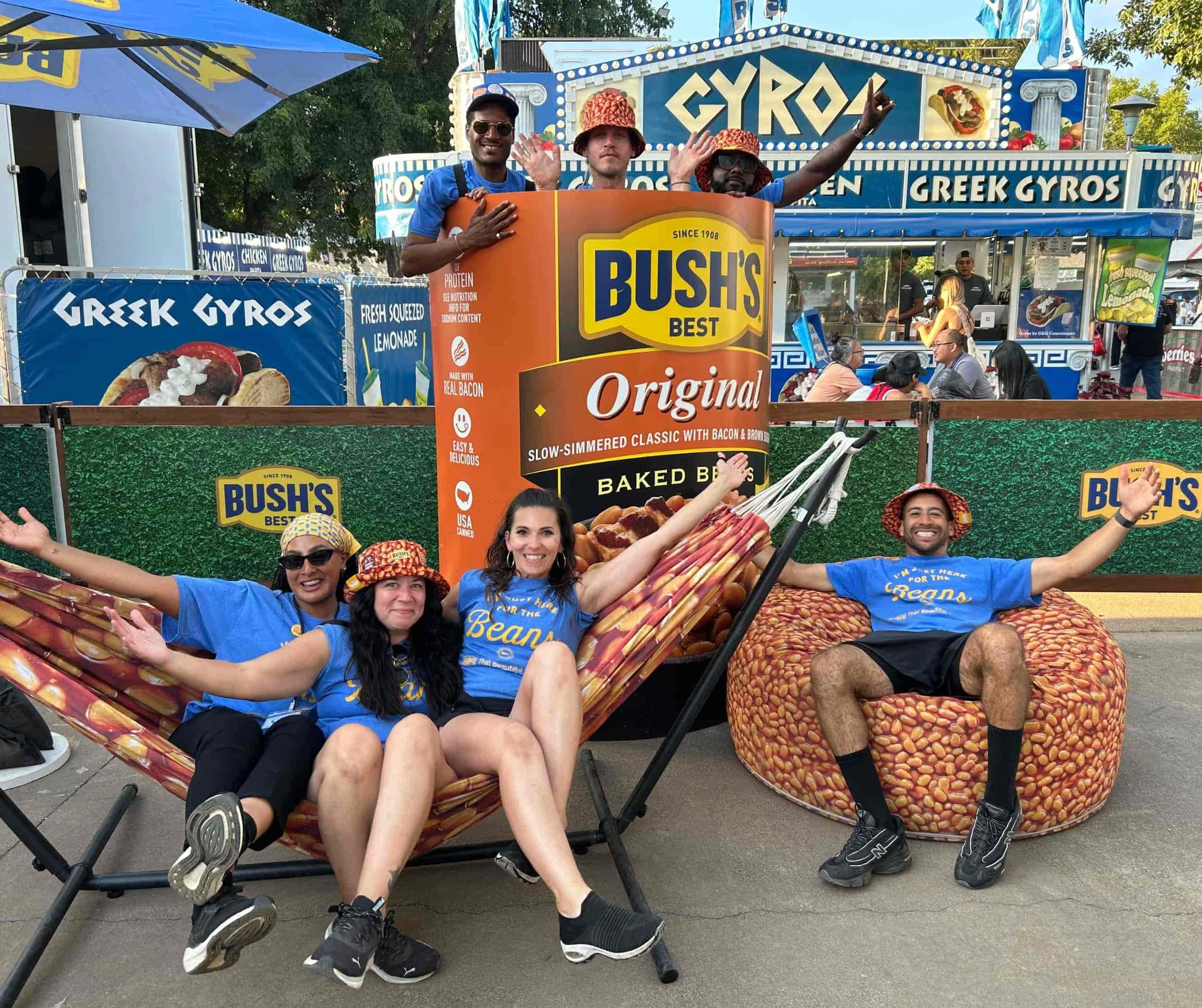 Event staff posing with giant Bush's Baked Beans can display, bean hammock, and beanbag at outdoor festival