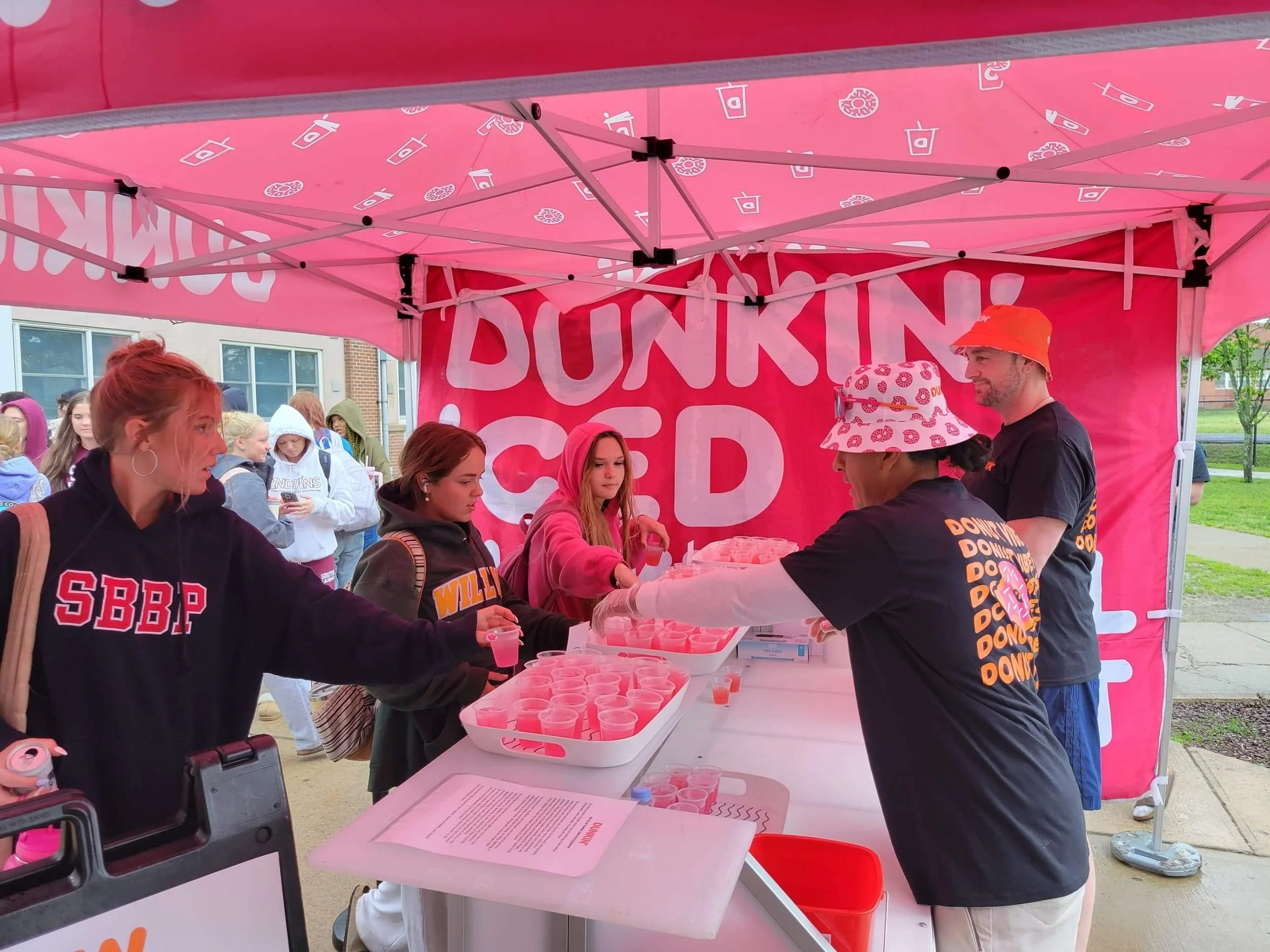 Dunkin staff serving free pink iced drink samples to students under a branded pink event tent