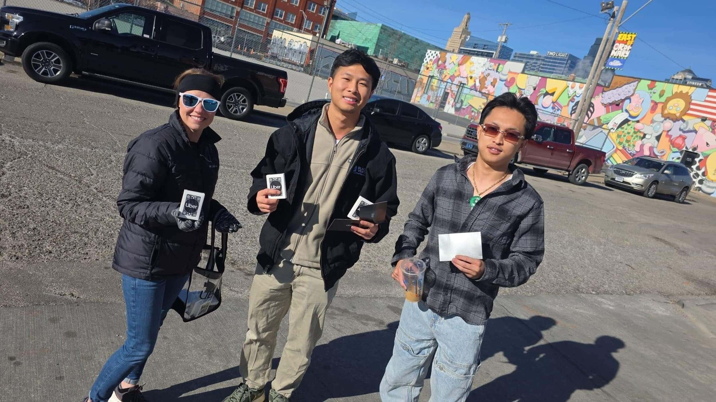 Three brand ambassadors holding Uber branded promotional materials and cards outdoors in a parking area.