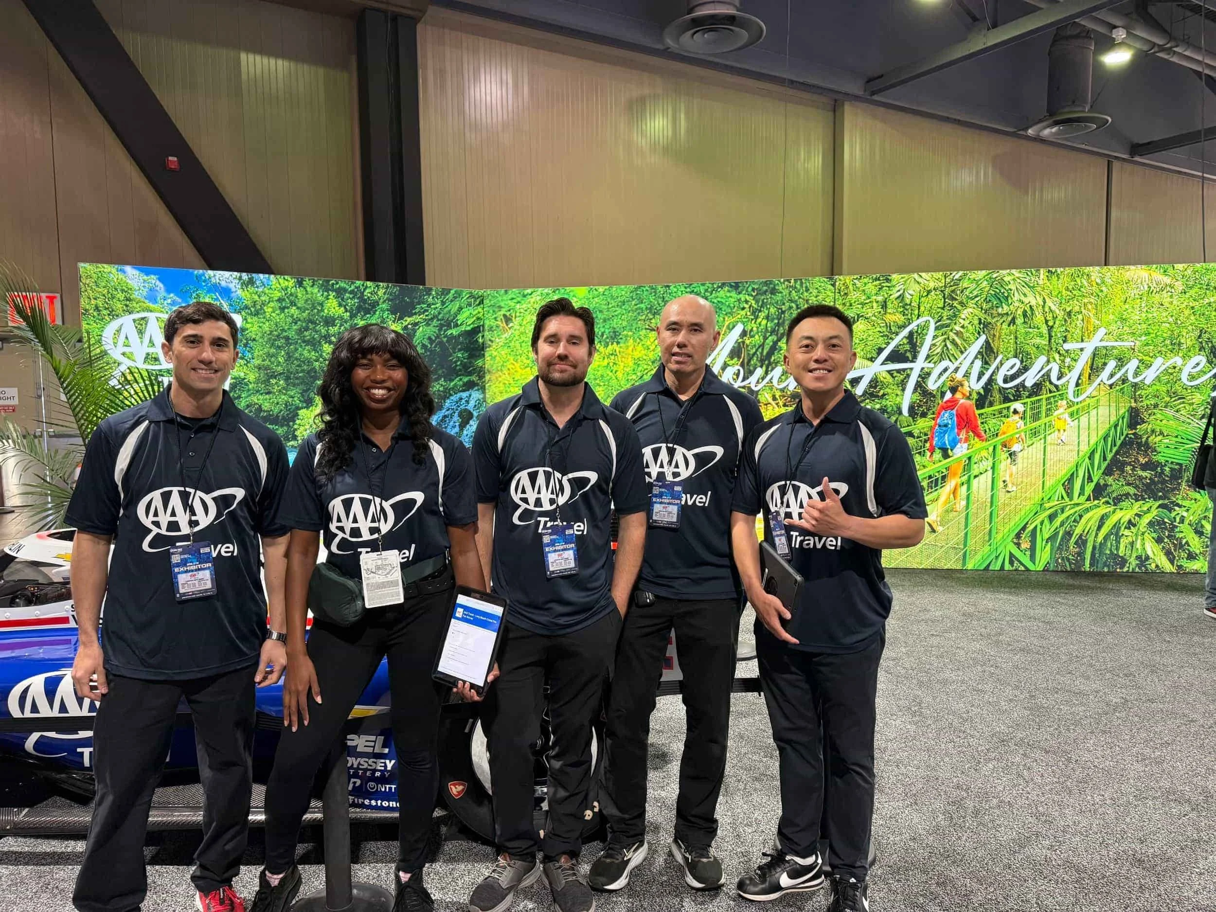 A group of AAA Travel staff posing in matching dark polo shirts at a trade show exhibit booth