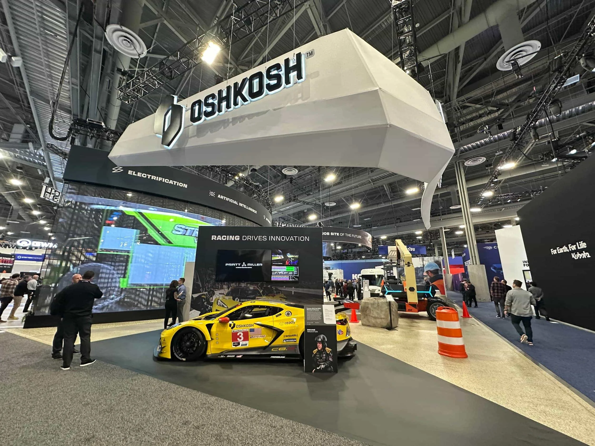 Yellow Pratt Miller Oshkosh Corvette sports car on display at an Oshkosh Corporation trade show booth