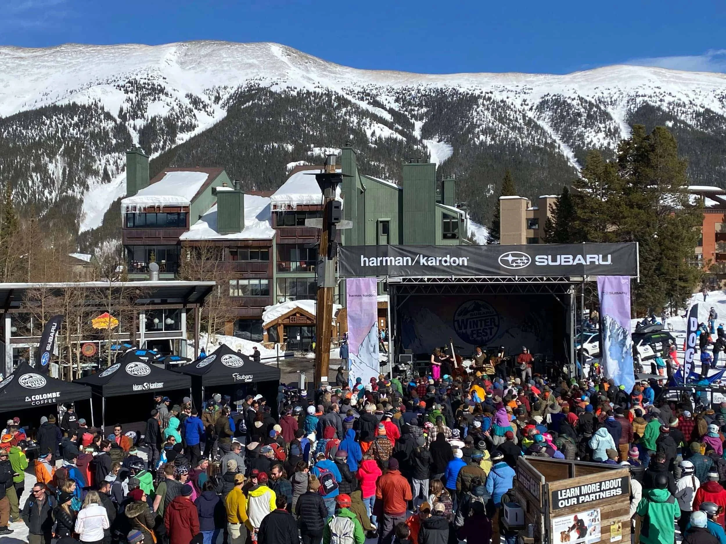 A large crowd attending a live concert at Subaru WinterFest stage in front of snow-capped mountains