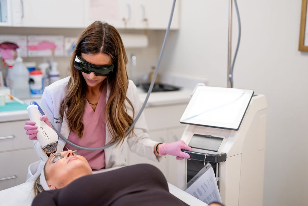 A CRNA wearing protective glasses and gloves performs a laser treatment on a patient in a medical clinic.