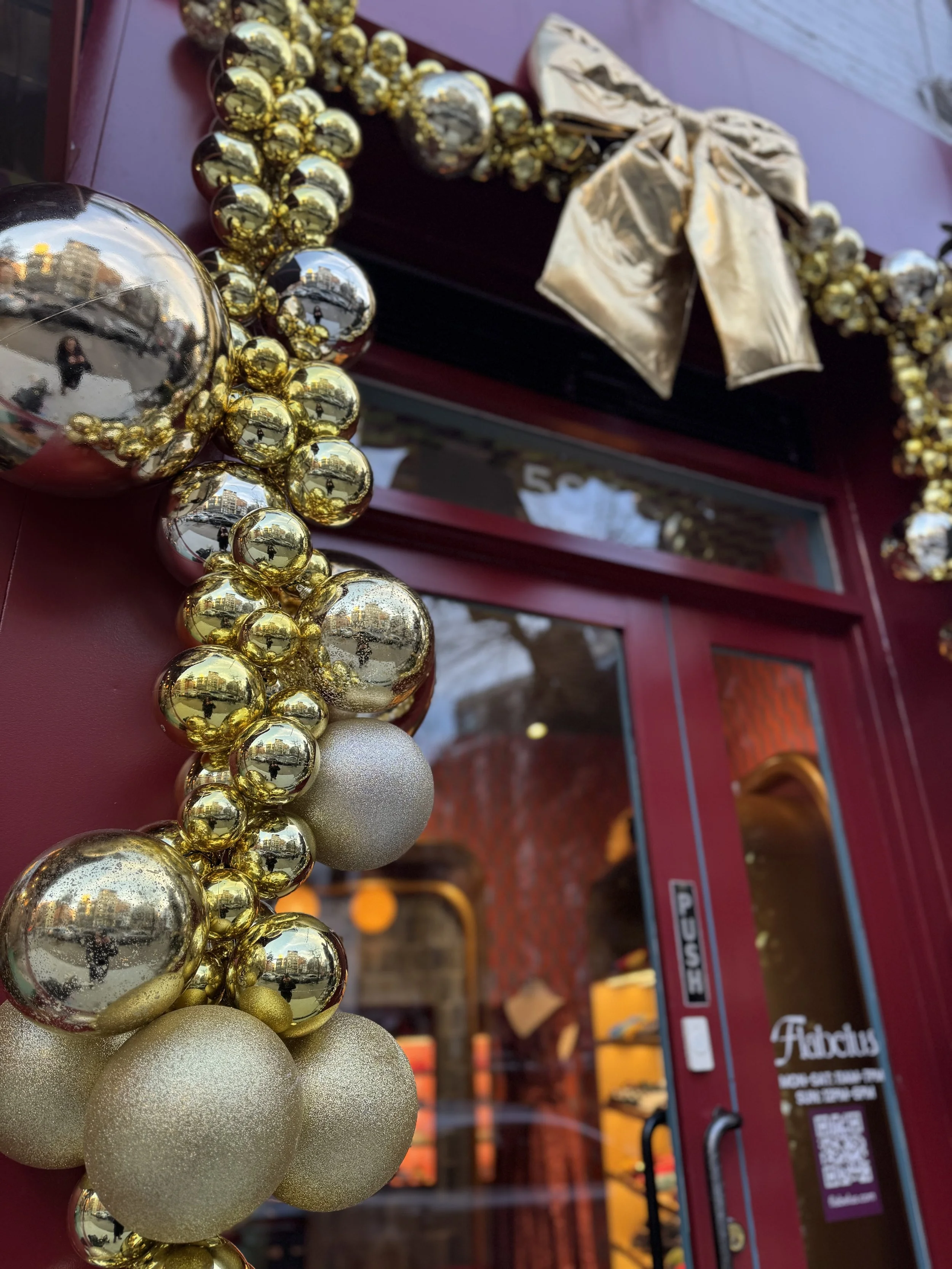 Close-up of gold and silver Christmas ornaments decorating a storefront with a fur-trimmed bow.
