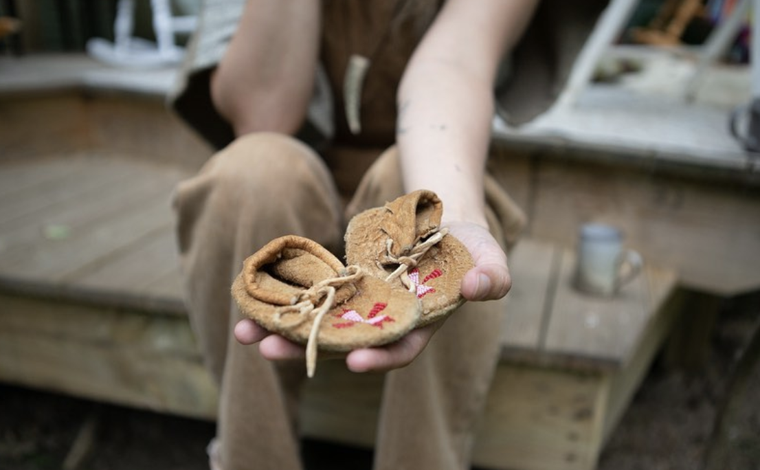 Person holding small, worn leather moccasins with red embroidery.