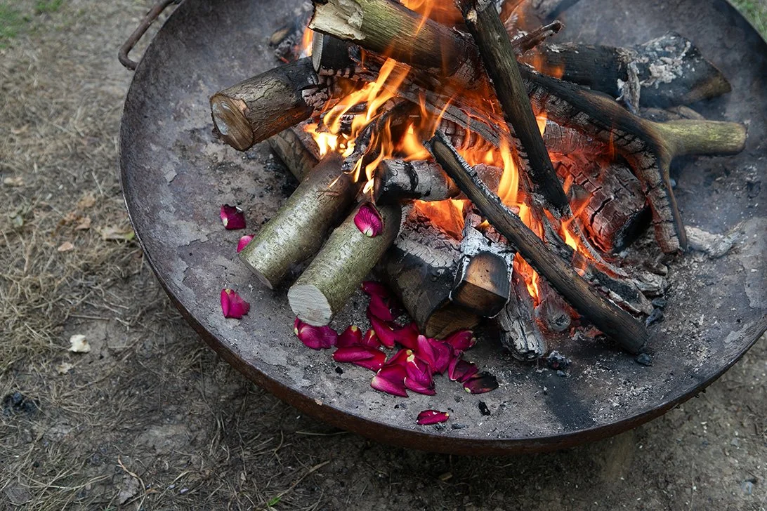 Outdoor fire bowl with burning logs and scattered rose petals.