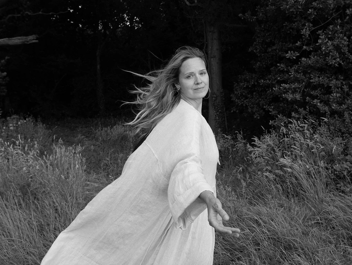 Black-and-white portrait of Katie Rose outdoors, reaching out with her hair blowing in the wind.