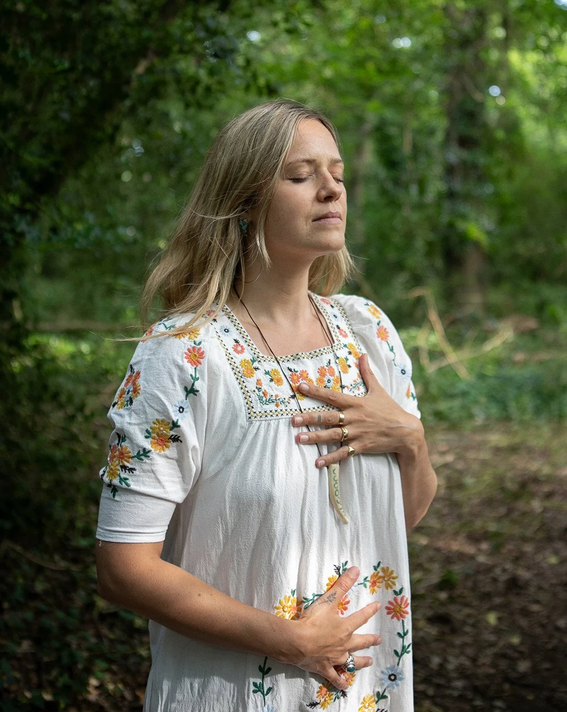Katie Rose in a calm woodland portrait, eyes closed with hands on her chest.