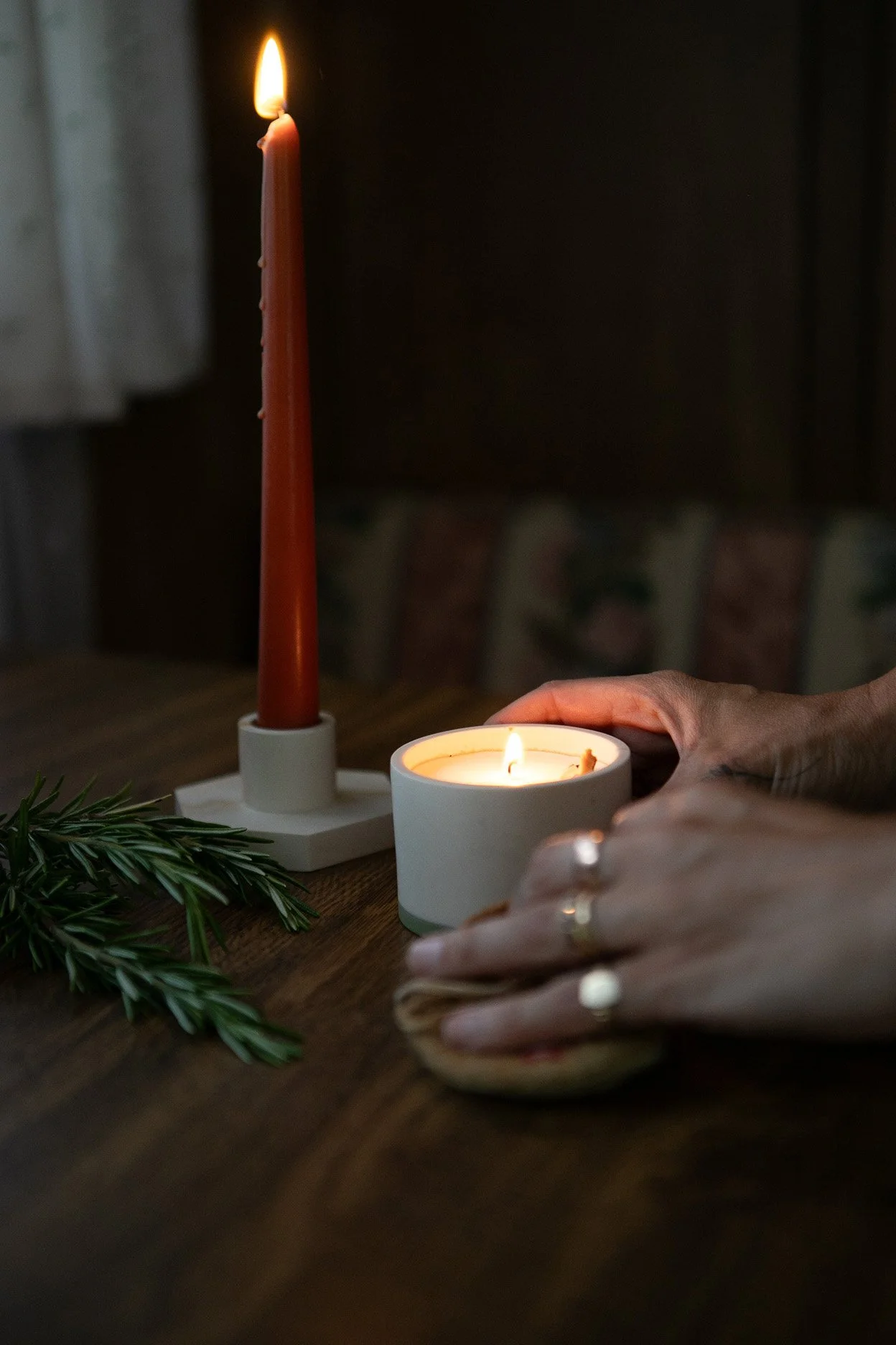 Lit candle on a table with hands resting beside it, creating a calm remembrance setting.