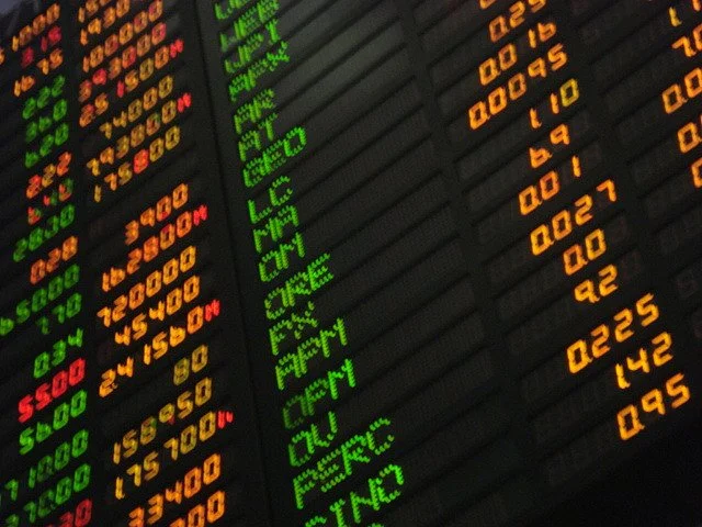 A close up image of a stock exchange stock ticker with green, orange and red letters and numbers.