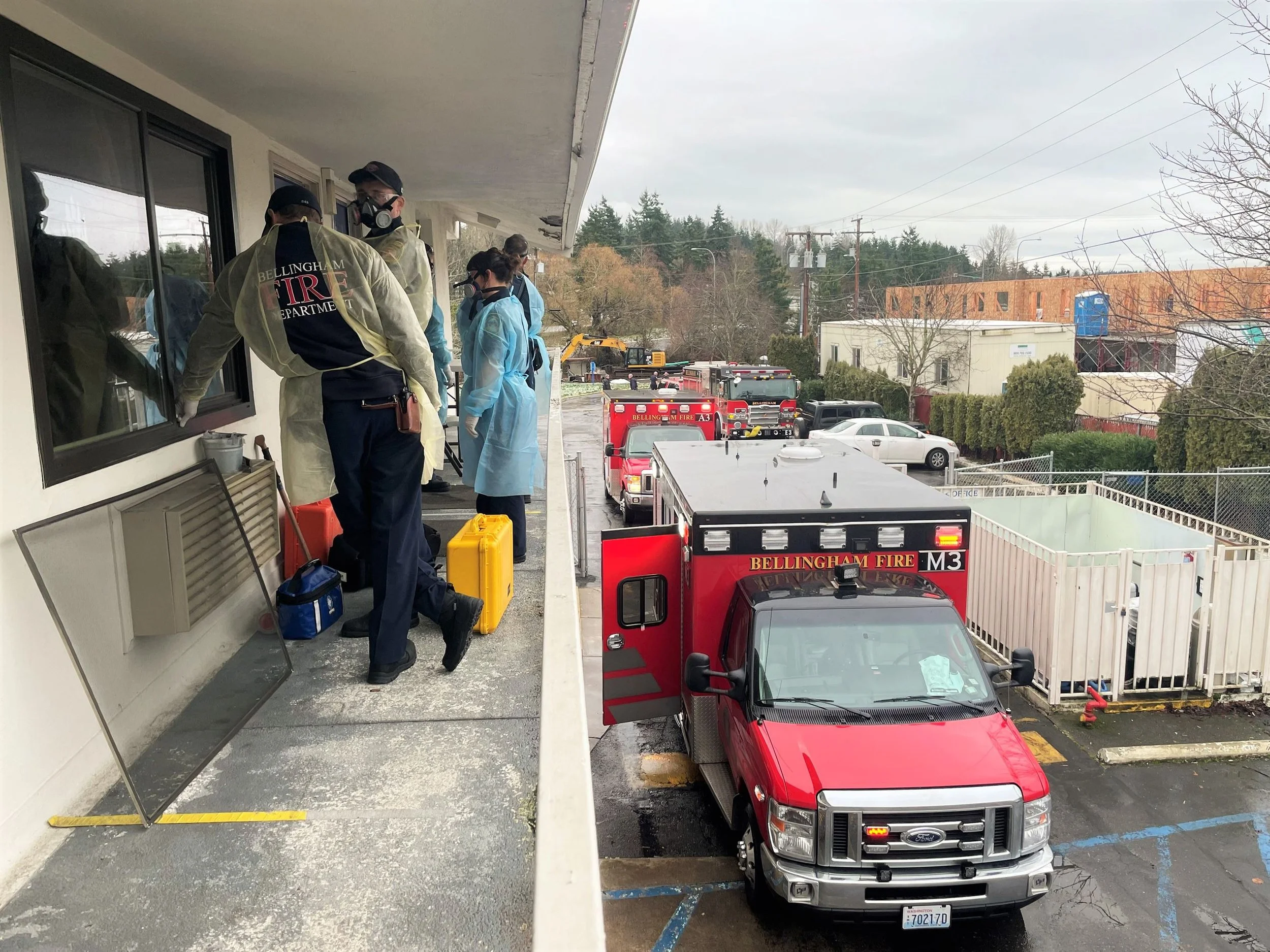 Members of the Bellingham fire department wearing respirators stand outside a room on the second story of a motel balcony.