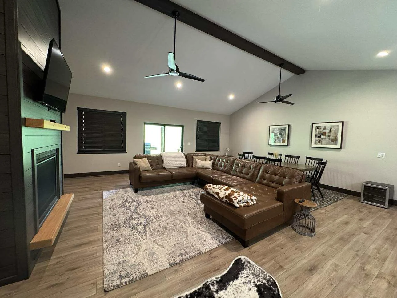 Spacious living room at Champagne & Ice vacation rental in Lead, South Dakota featuring a leather sectional, modern fireplace, dining area, and vaulted ceiling with exposed beams.