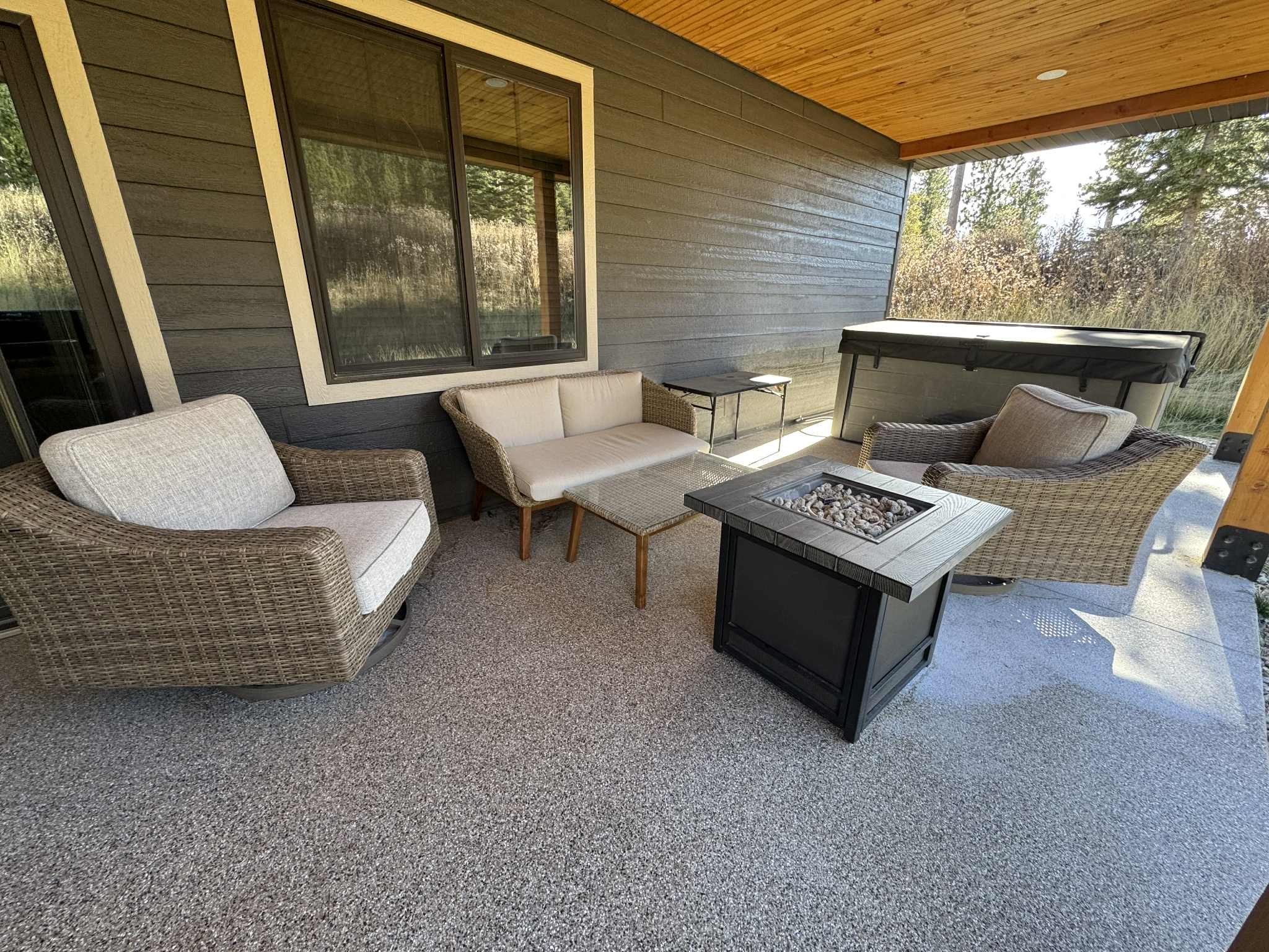 Covered patio at Champagne & Ice vacation home in Lead, South Dakota featuring wicker lounge chairs, a fire table, and a private hot tub.