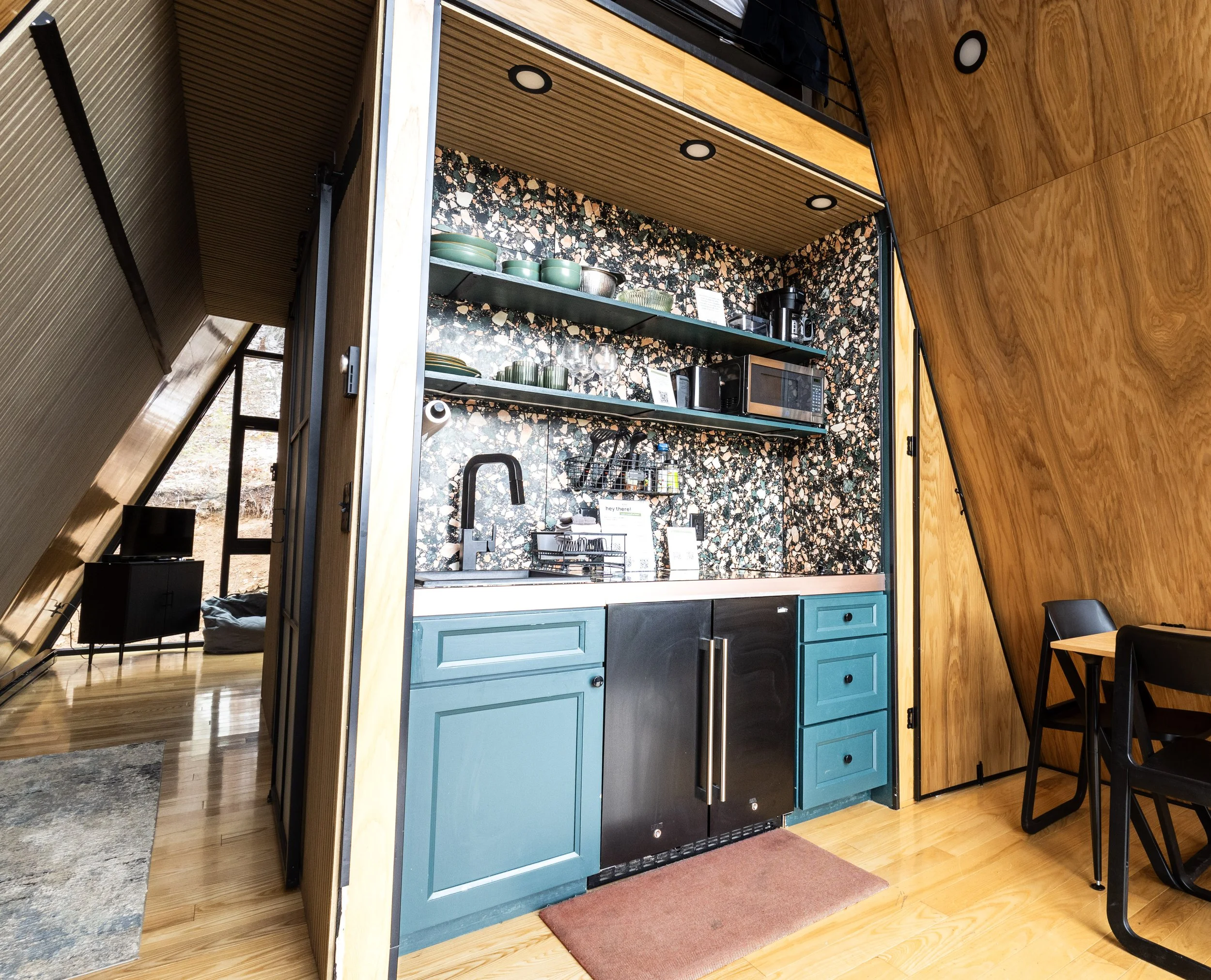 Modern kitchenette inside A-frame cabin with sink, mini fridge, and open shelving in the Black Hills near Lead South Dakota