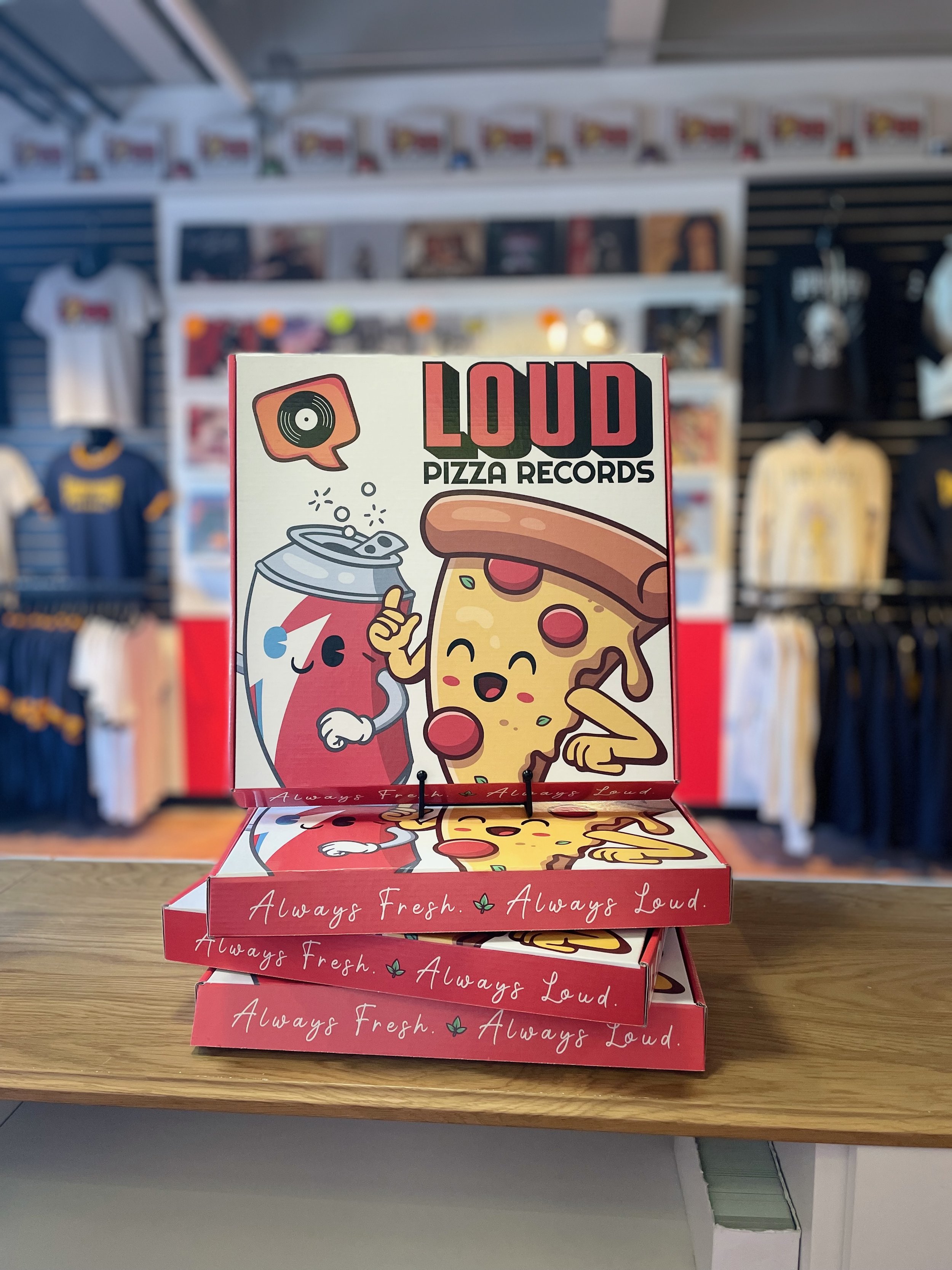Stacks of pizza-themed pizza records boxes with cartoon pizza slice and soda illustrations, in a retail store.
