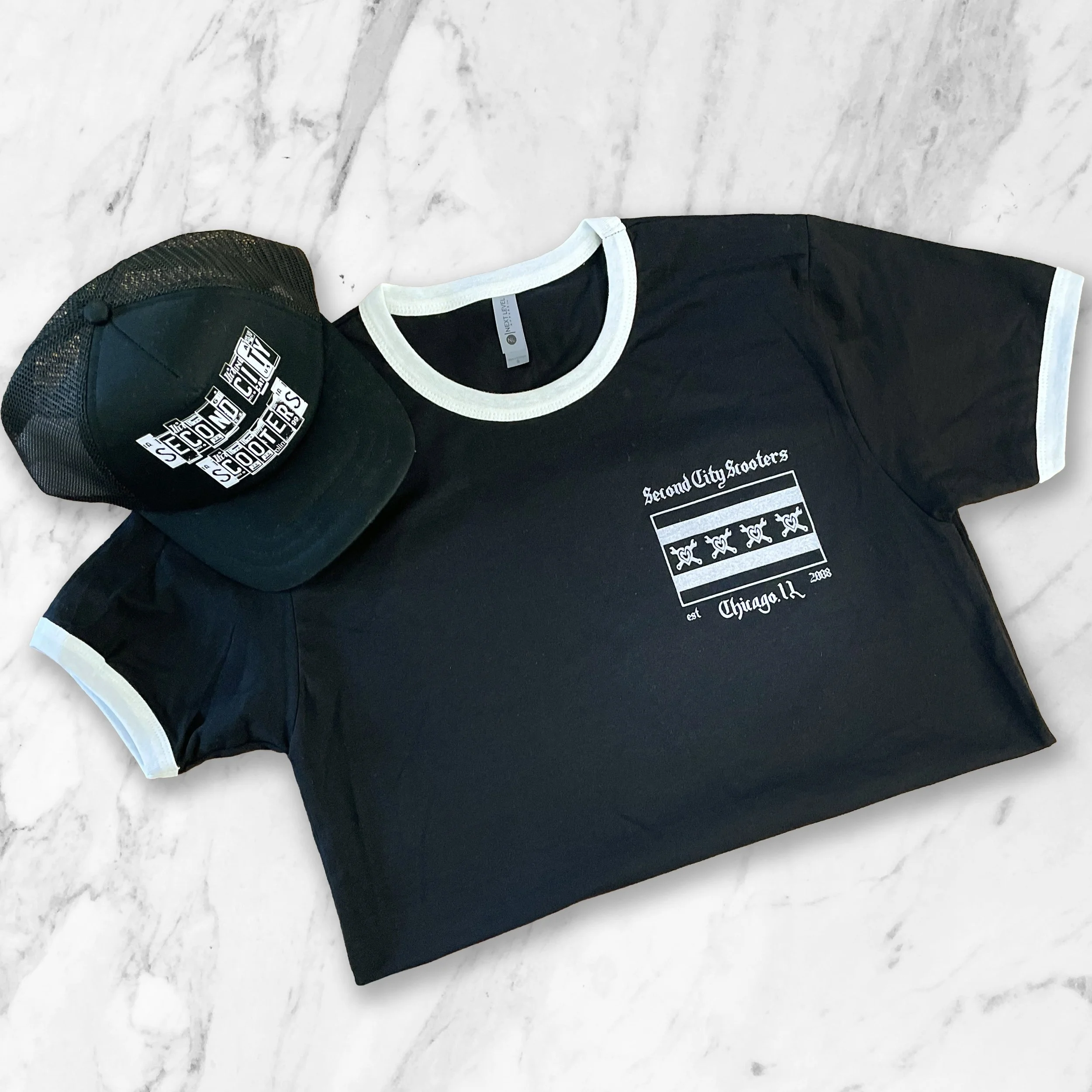 Black t-shirt with white trim and a graphic design in white on the front, and a black trucker hat with a graphic design in white on the front, both placed on a white marble surface.