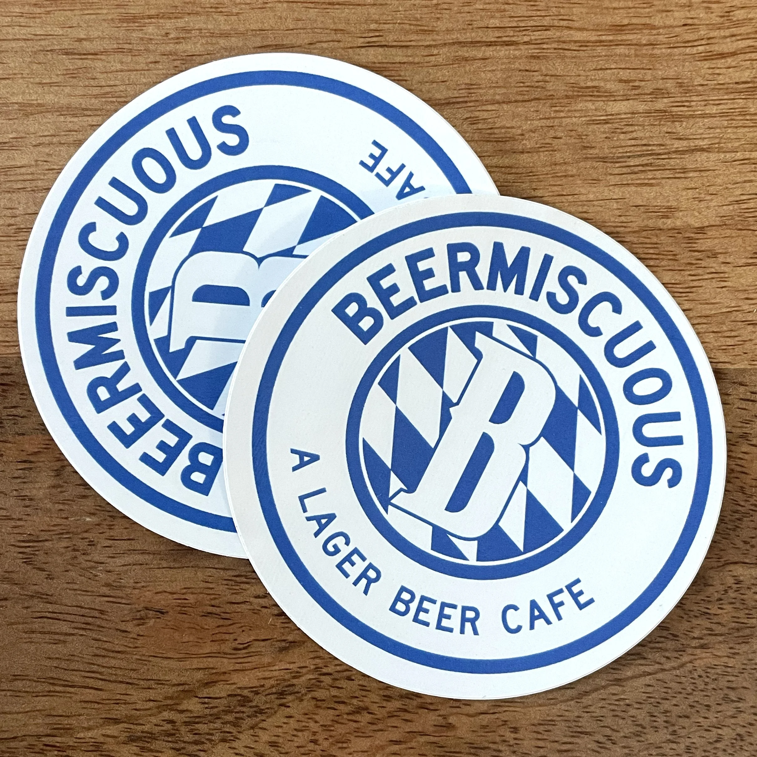 Two circular stickers with a blue and white logo for Beermiscuous, a lager beer cafe. The logo includes a stylized beer mug and a pattern of diagonal stripes.