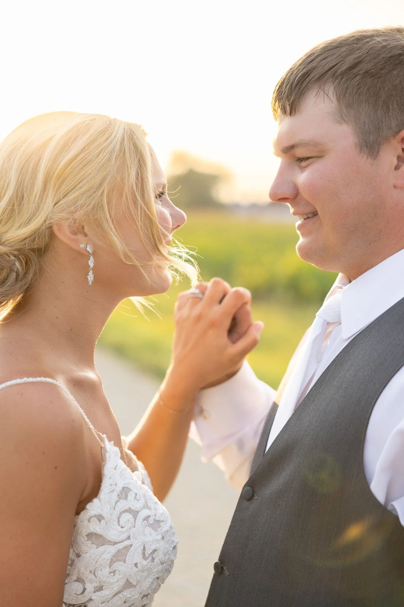 A bride and groom sharing a tender moment outdoors, holding hands and smiling at each other during sunset.