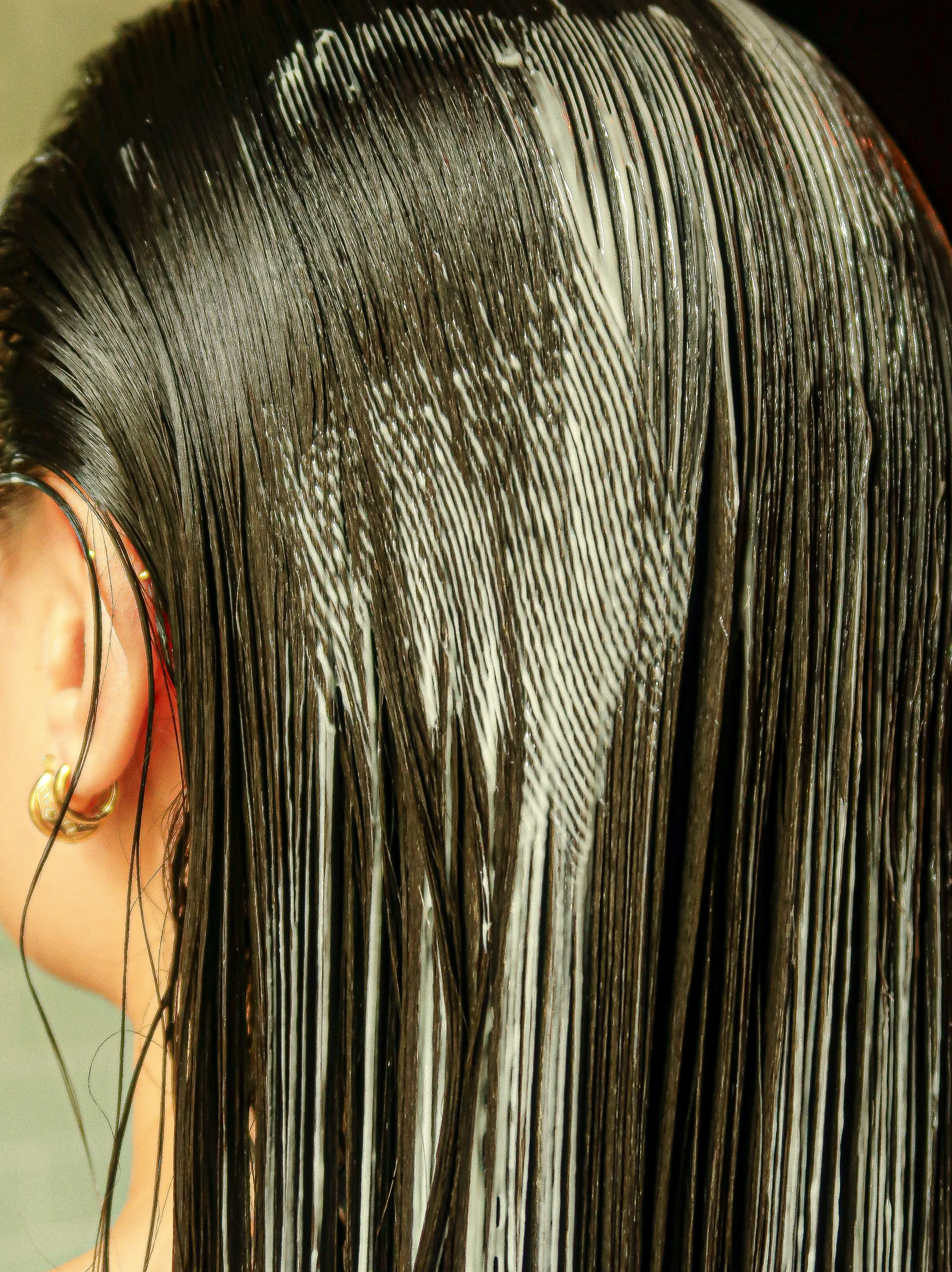 Close-up of a person's head with wet, black hair combed straight back.