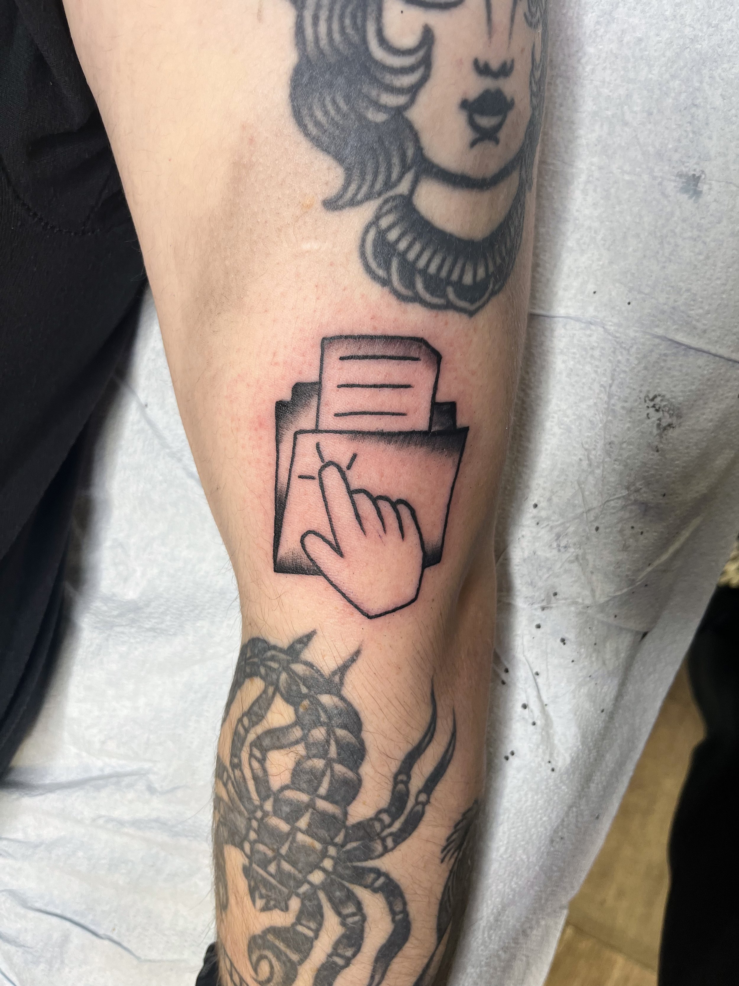 Tattoo of a woman's face with styled hair and dark lips above a tattoo of a chain link design on a person's arm.