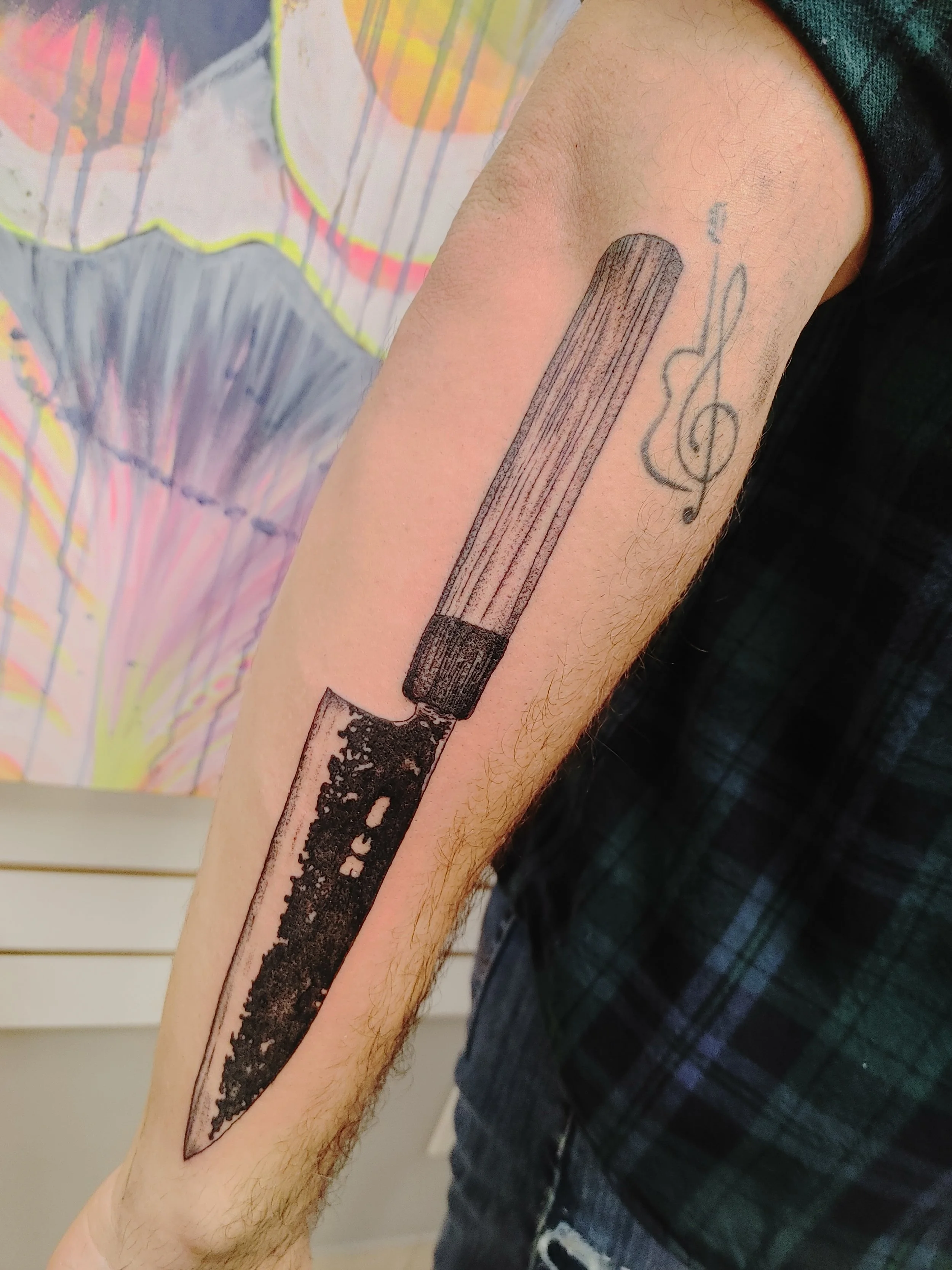 A tattoo of a black popsicle with a stick, and a musical note, on a person's arm.
