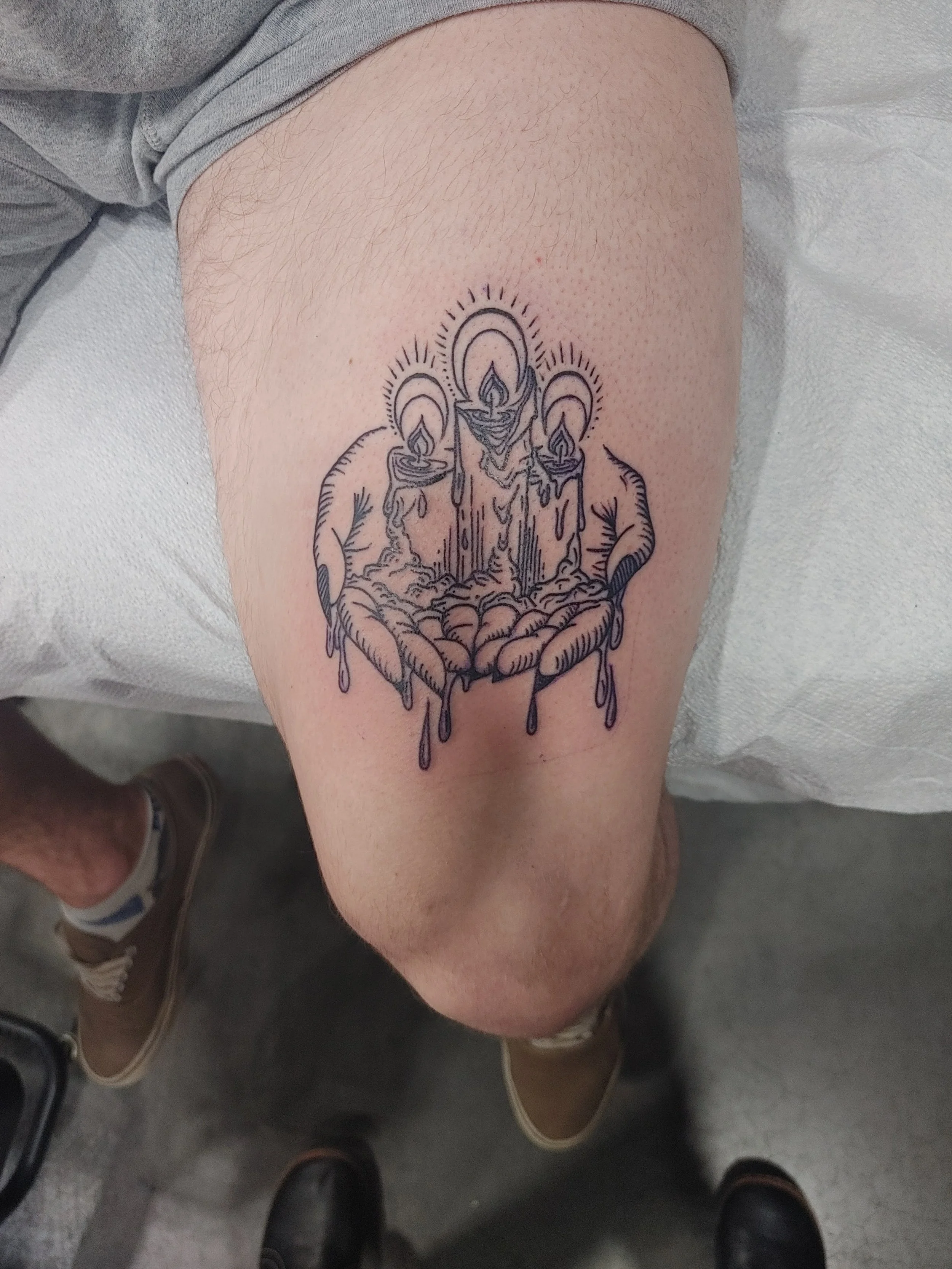 Tattoo of three candles burning above an open hand on a person's upper thigh.