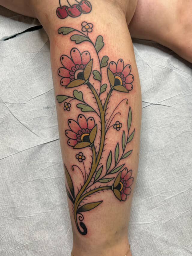 Colorful floral tattoo on a person's leg with pink, yellow, black, and green details.