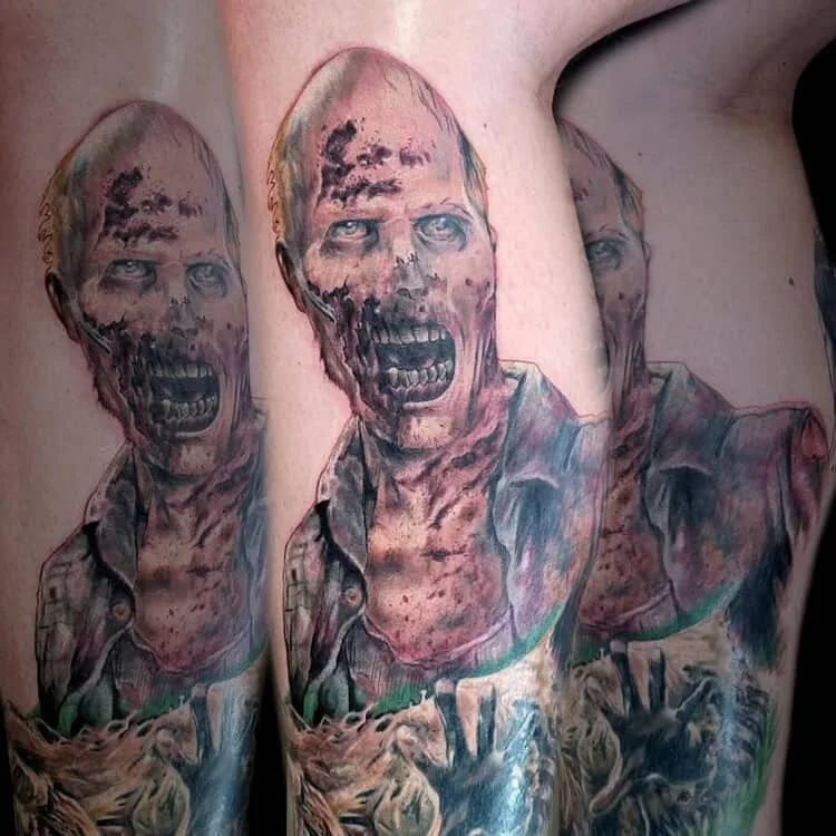 Tattoo of a screaming zombie-like figure with exposed skull and decayed skin, wearing a checkered shirt and reaching out with skeletal hands.