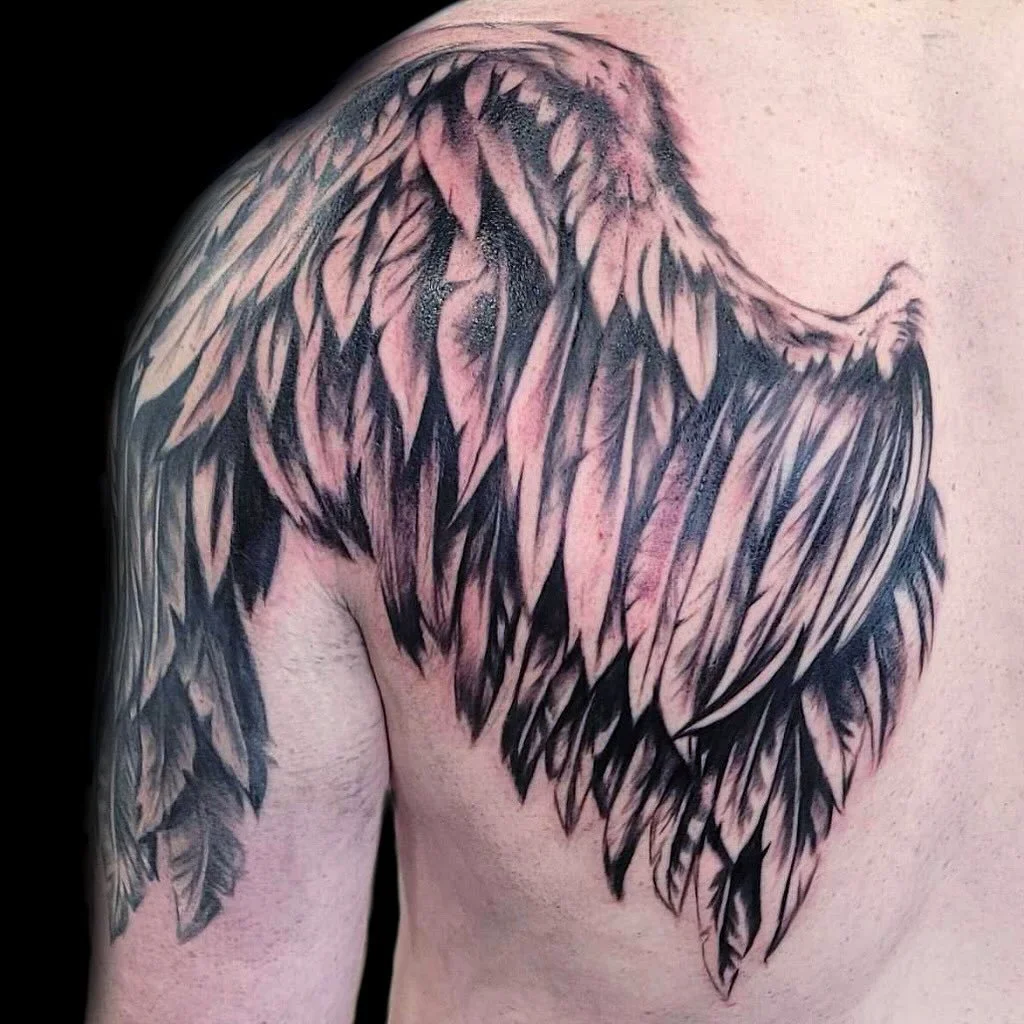 Tattoo of angel wings on a person's shoulder, with detailed black and pink shading.