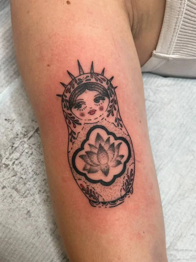 Tattoo of a stylized Madonna with a halo and a lotus flower on the body on a person's forearm.