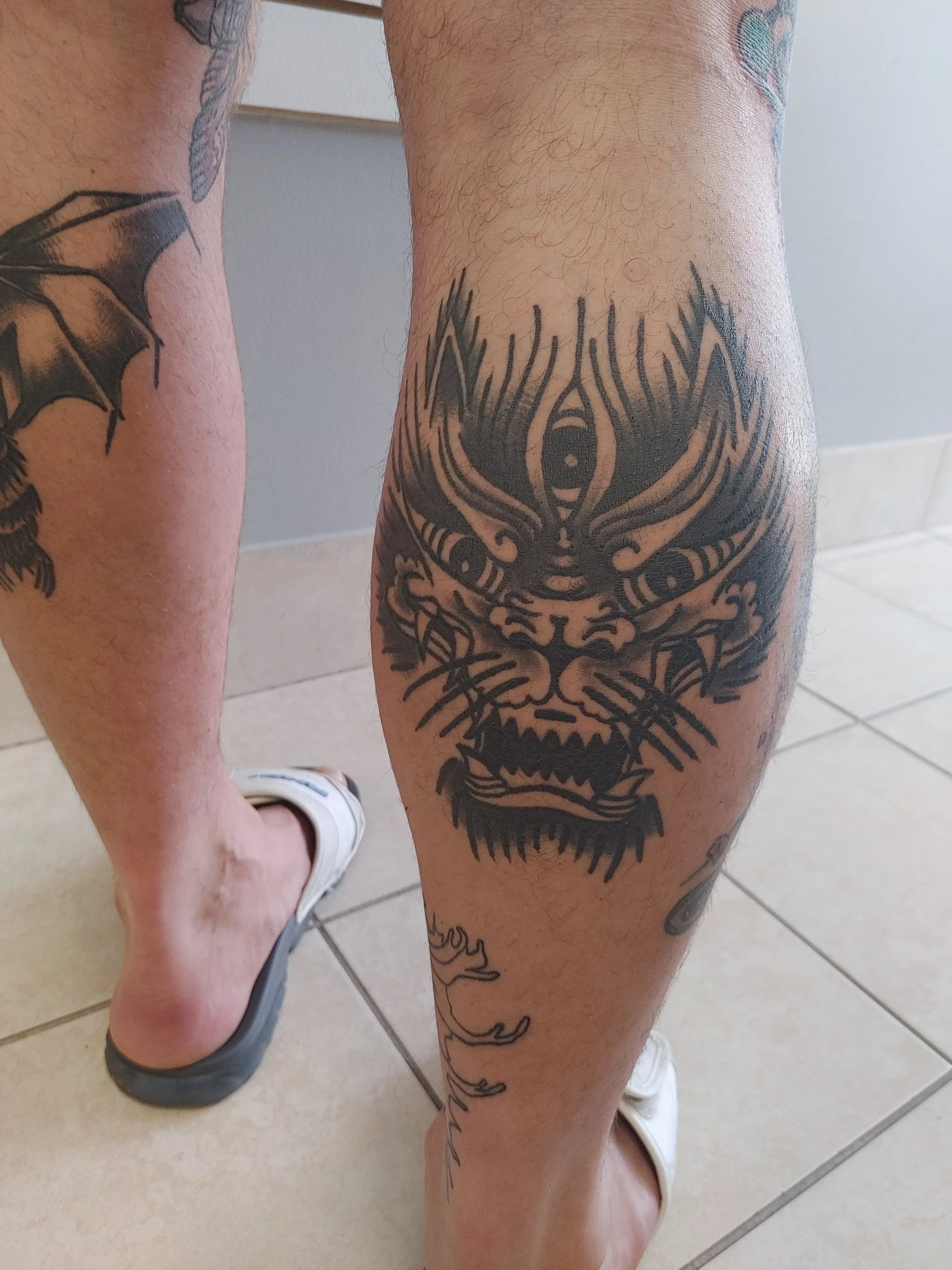 Close-up of a person's leg with a large tattoo of a tree with a face and abstract features.