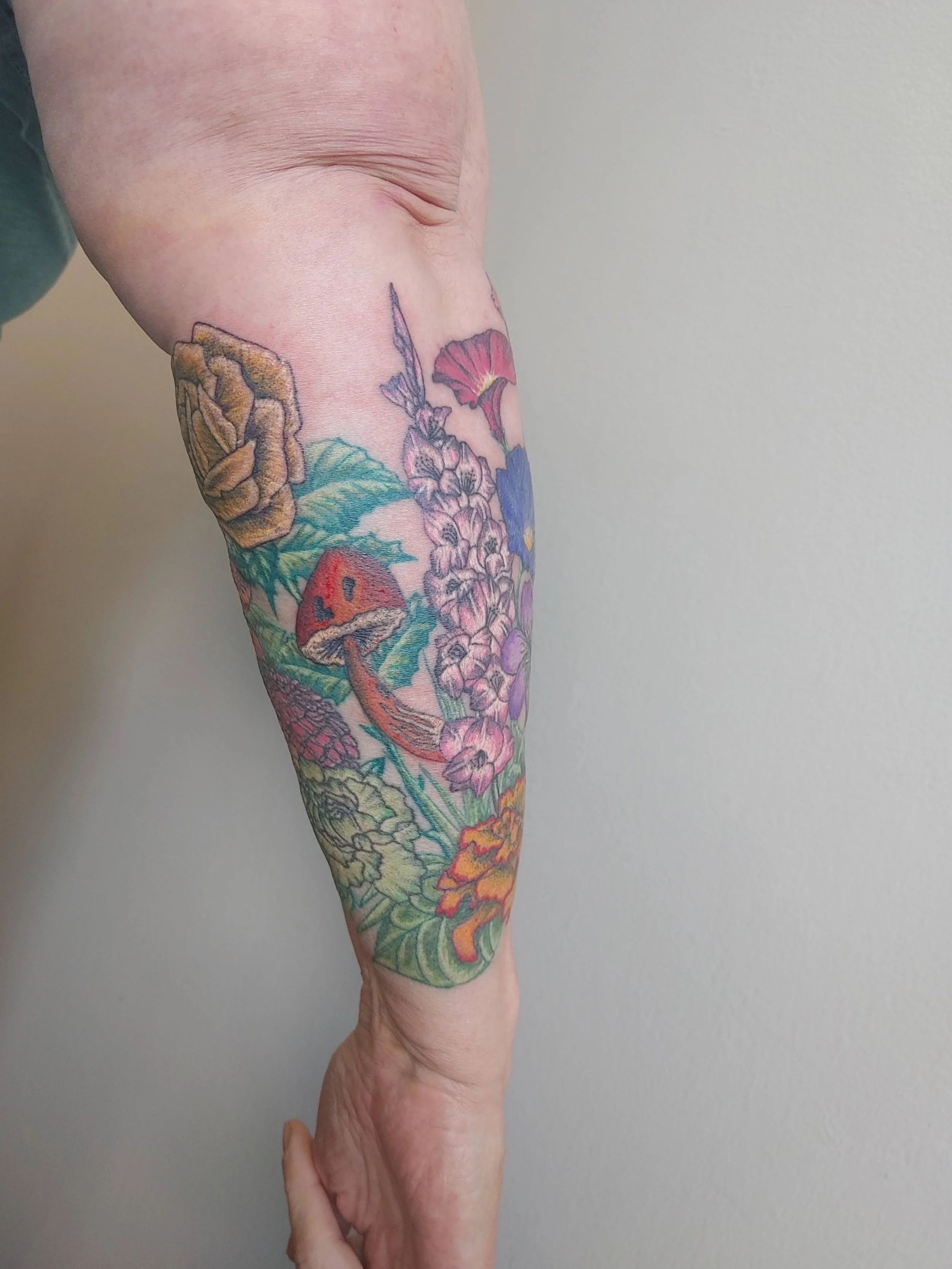 A person's forearm covered in a colorful floral tattoo featuring flowers, leaves, and a ladybug.