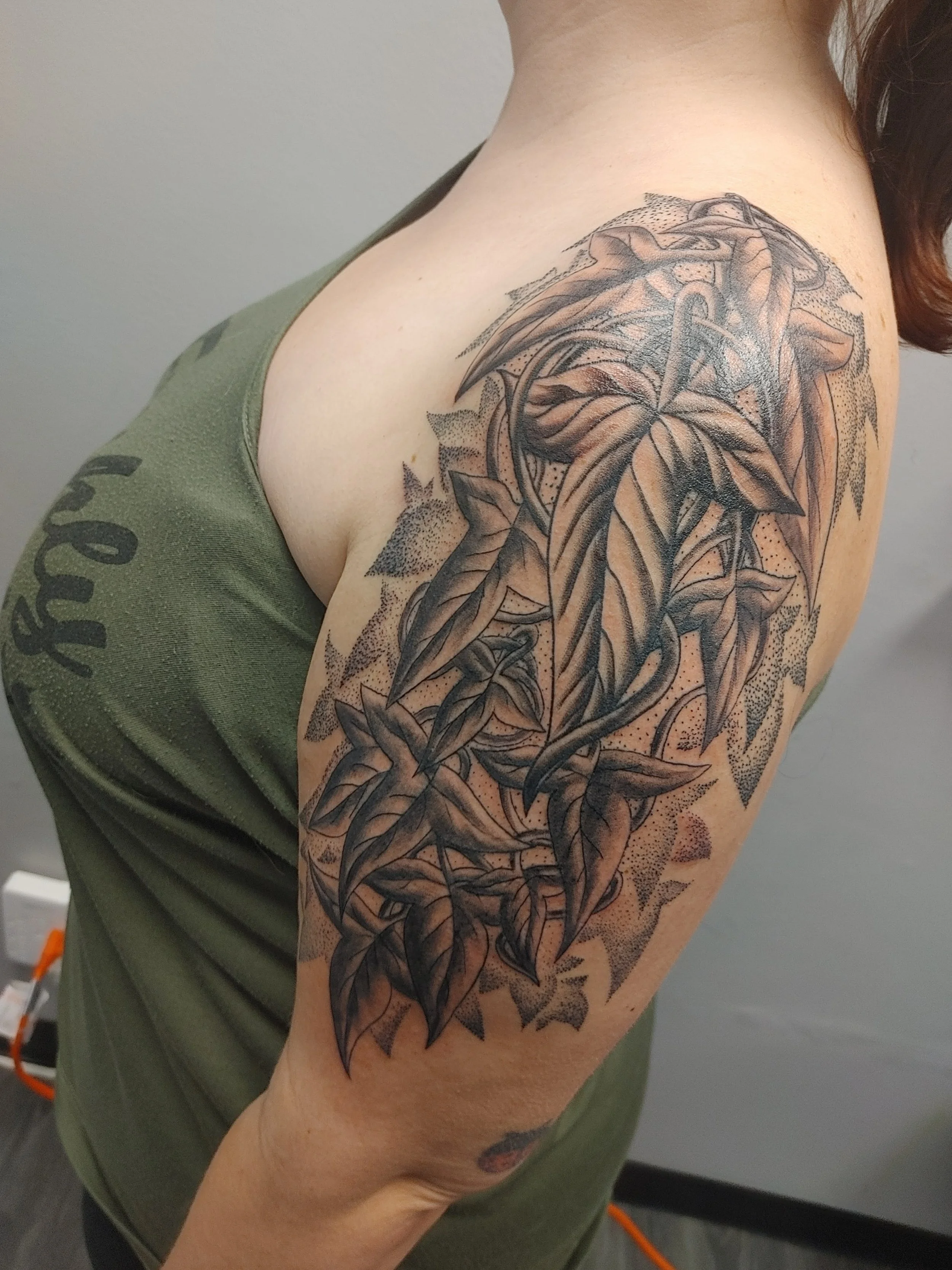 Tattoo of a lion's face with leaves and intricate details on a person's upper arm and shoulder.