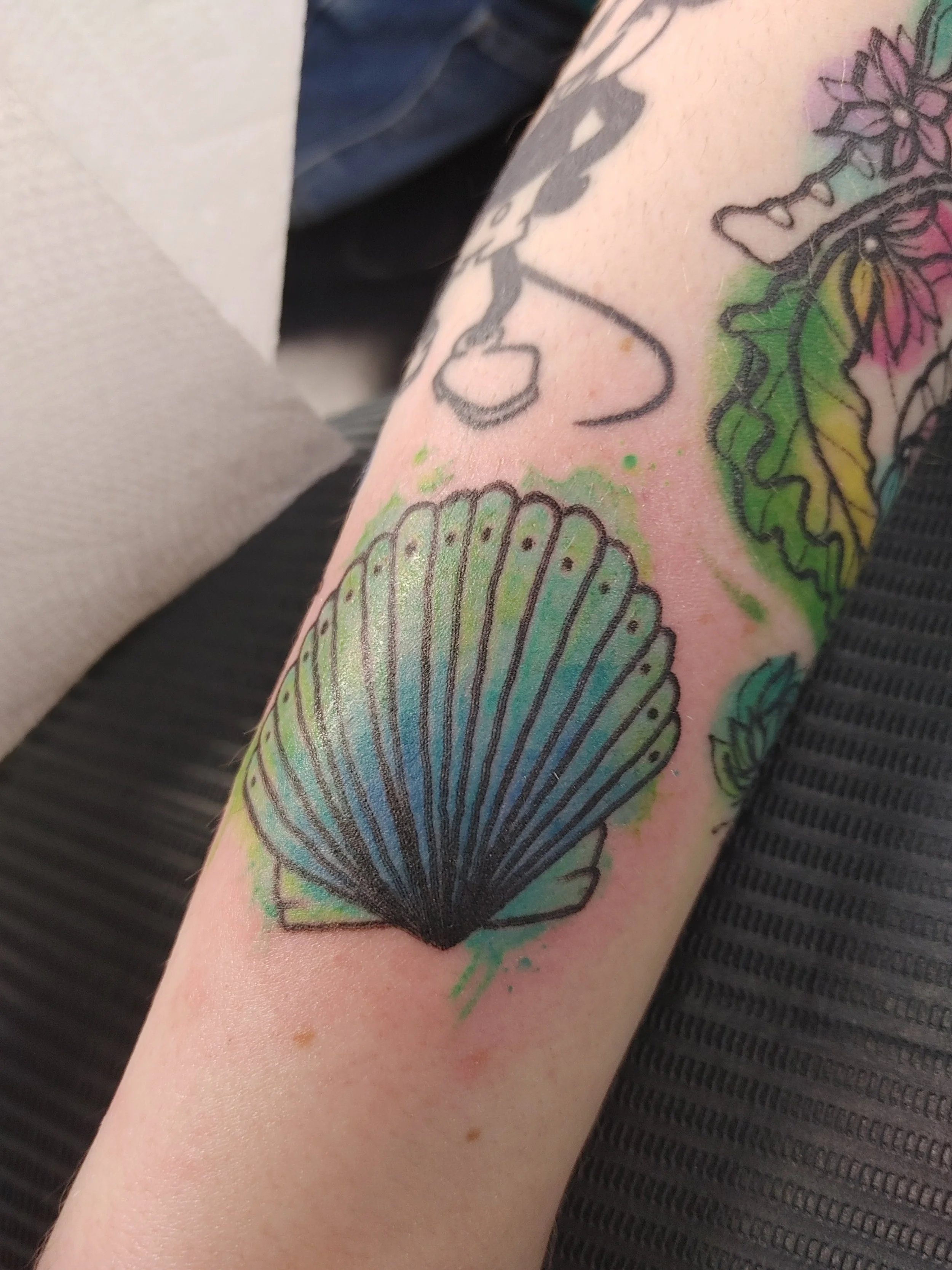 Colorful butterfly tattoo on person's arm with green, pink, and blue hues.