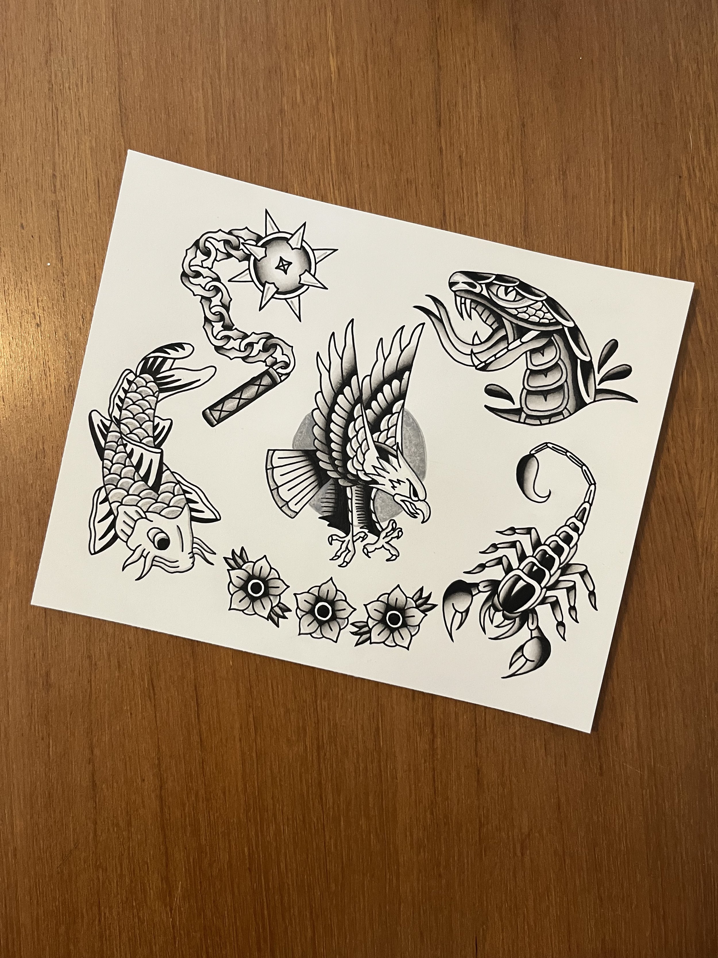 Black and white tattoo-style drawing featuring a koi fish, a bird with dragonfly wings, a snake, and floral designs, all arranged in a circular pattern.