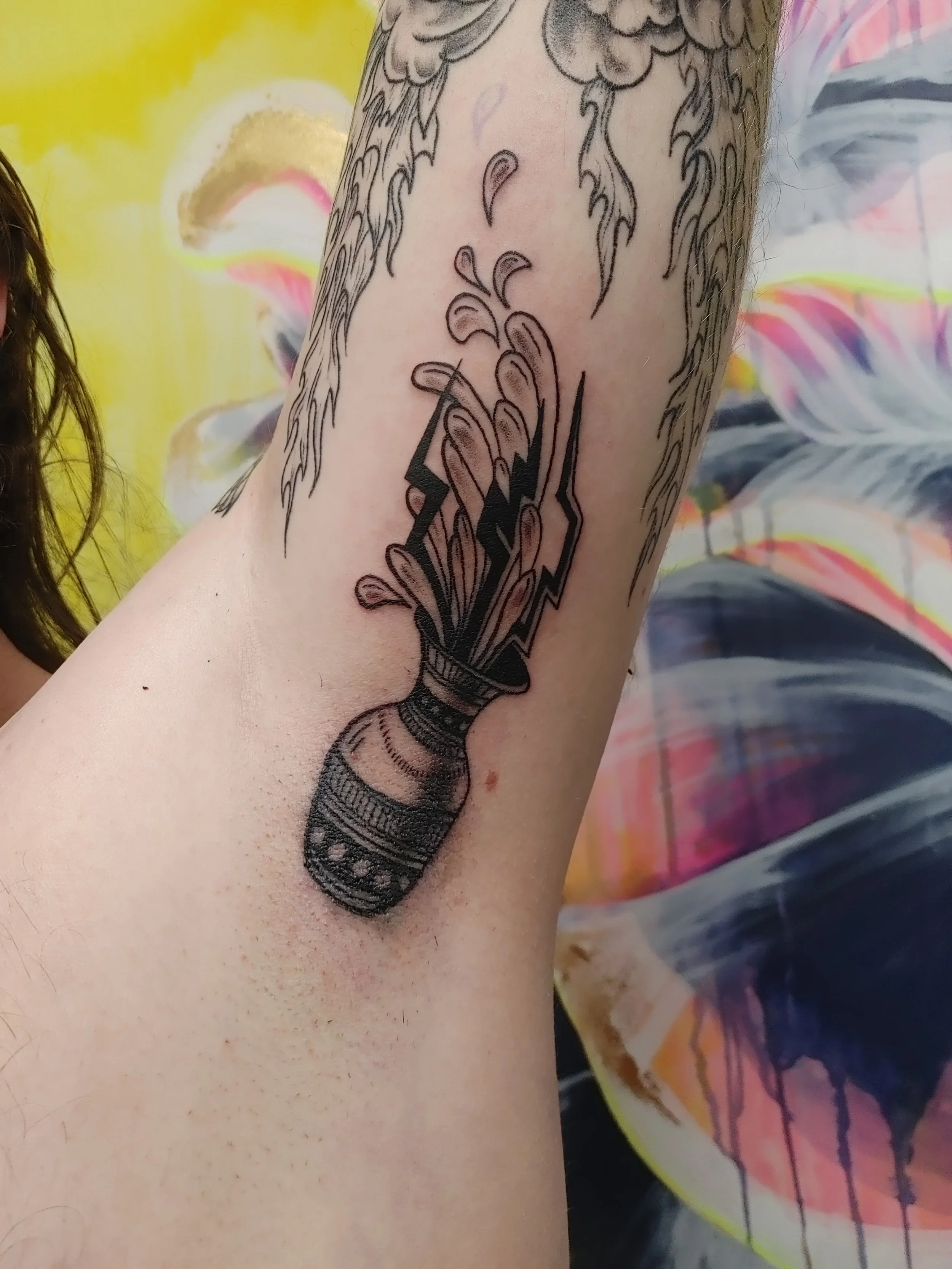 Black tattoo of a dagger with a floral design on the forearm of a person.