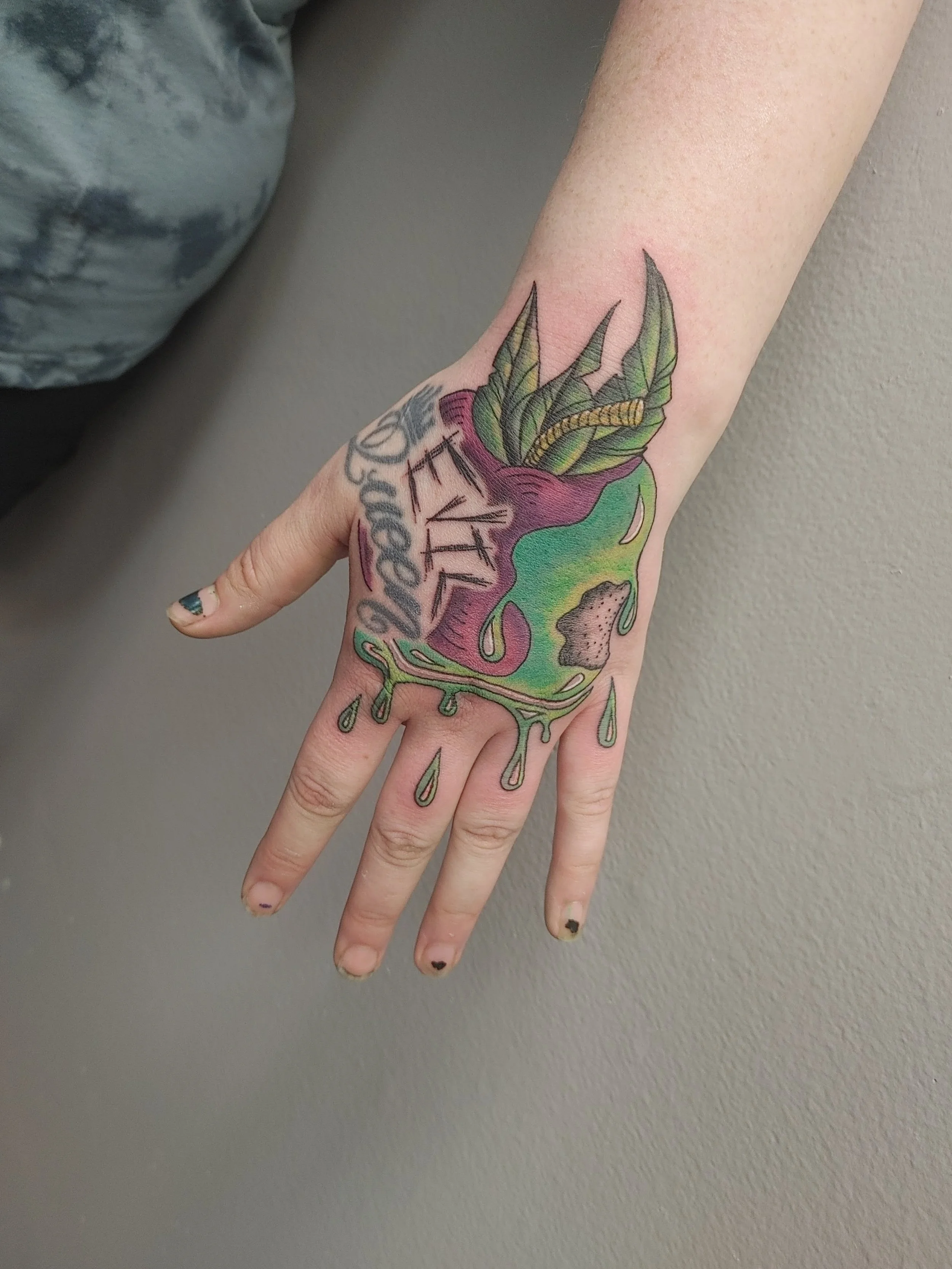 A person's hand with tattoos featuring a colorful illustration of a heart with leaves, a caterpillar, and the word 'LOVE' on the wrist.
