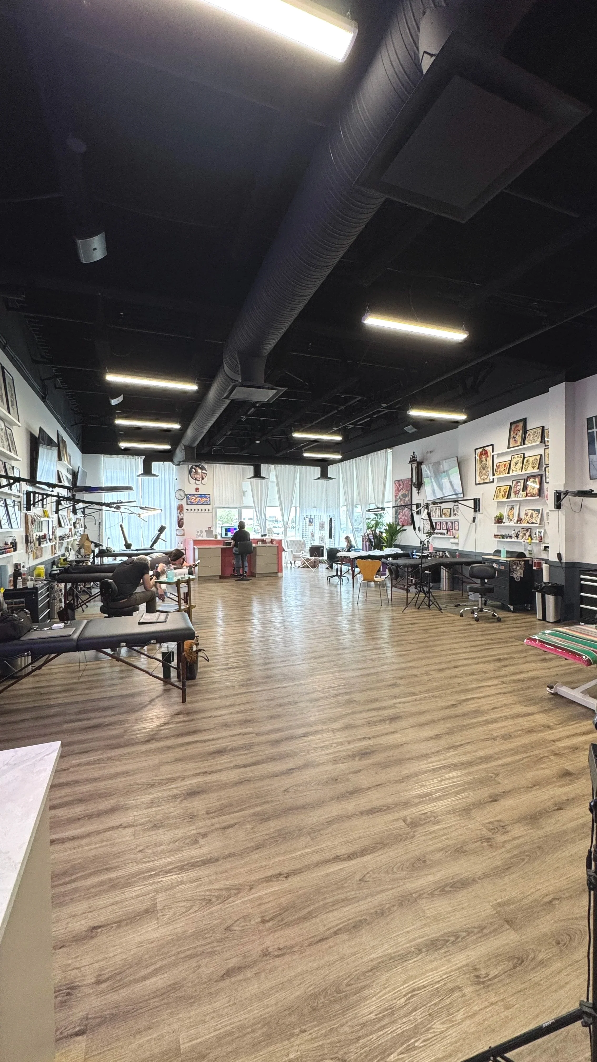 Interior view of a tattoo studio with tattoo workstations, artwork on the walls, and a few clients getting tattoos.