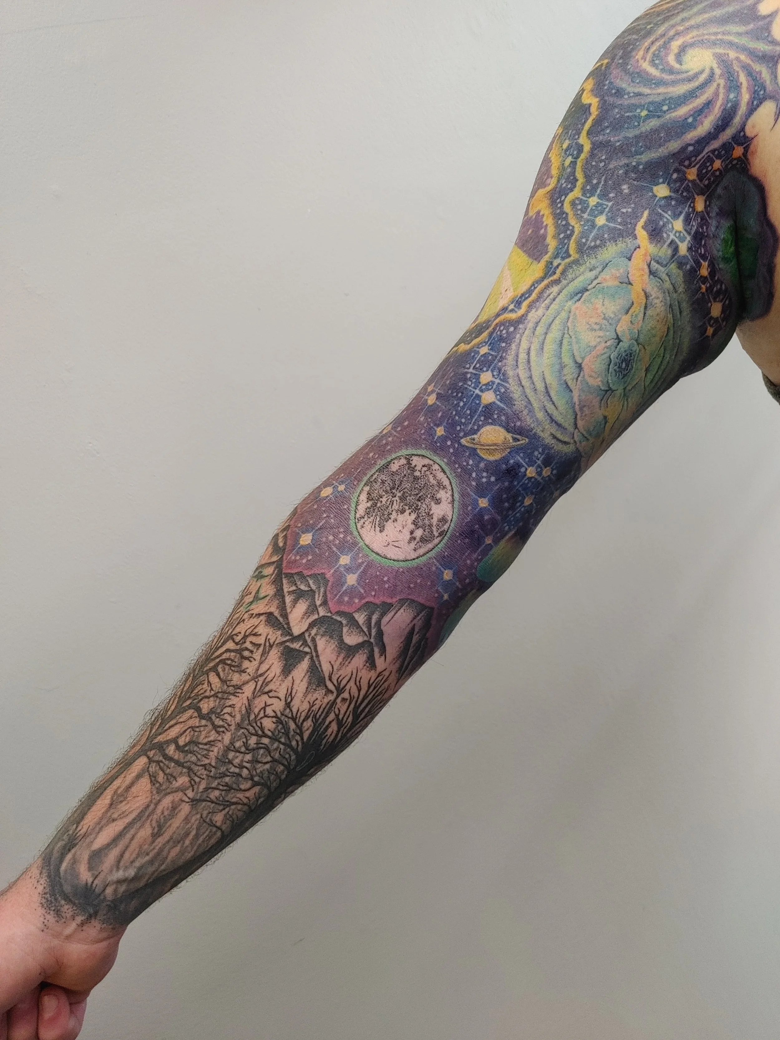 A person's arm covered in a colorful galaxy-themed tattoo with various celestial elements and patterns.
